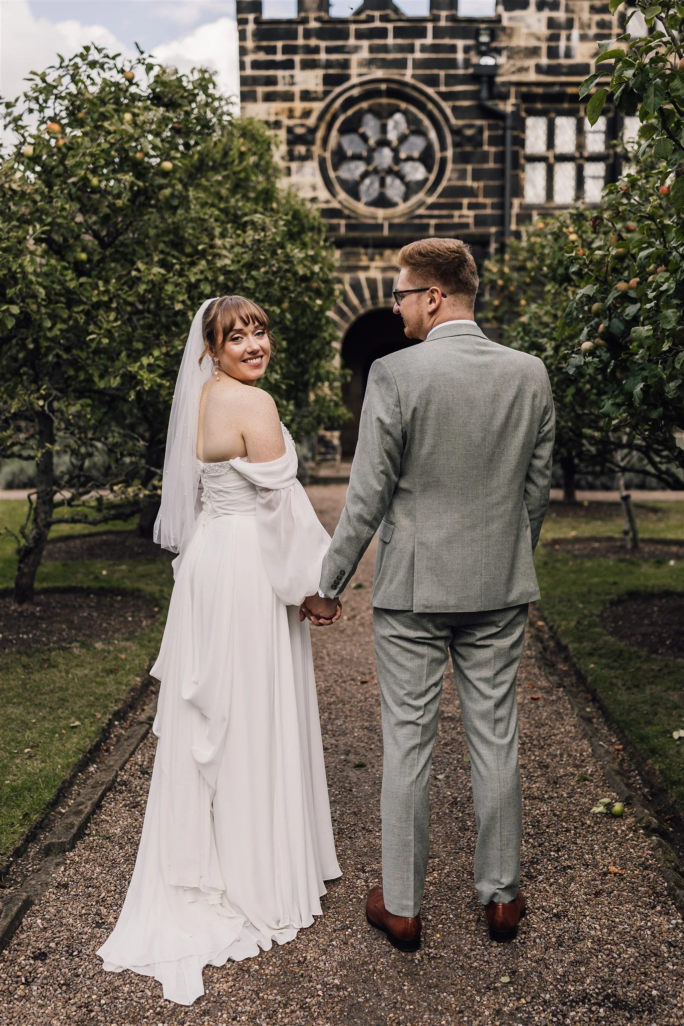 Bride and groom walking through gardens at East Riddlesden Hall with historic building backdrop