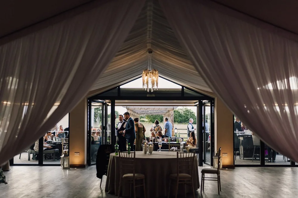 The barn reception room with white draping, chandeliers and the courtyard beyond