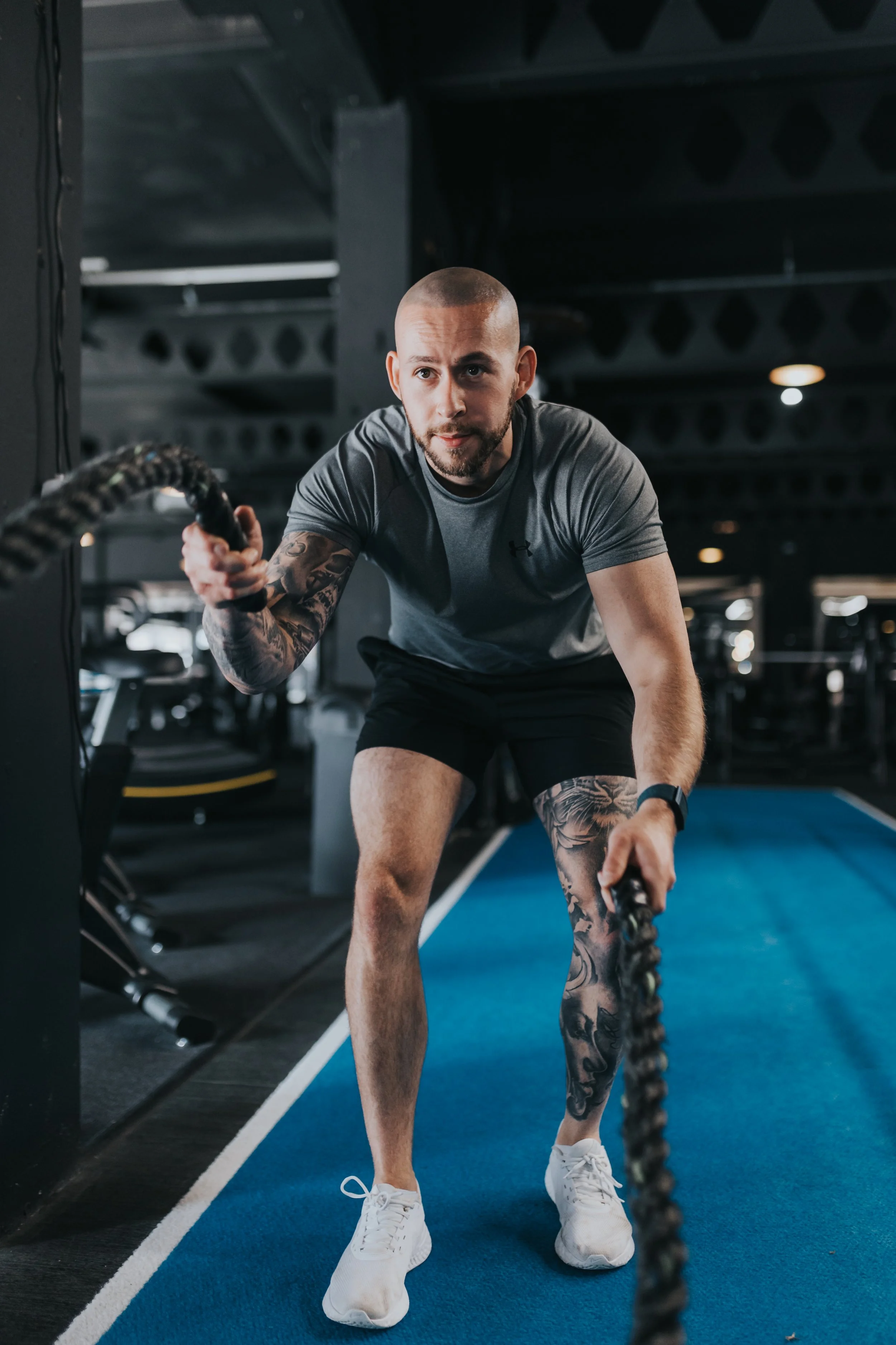 Man performing a battle rope exercise in a gym with dark interior and exercise equipment in the background.