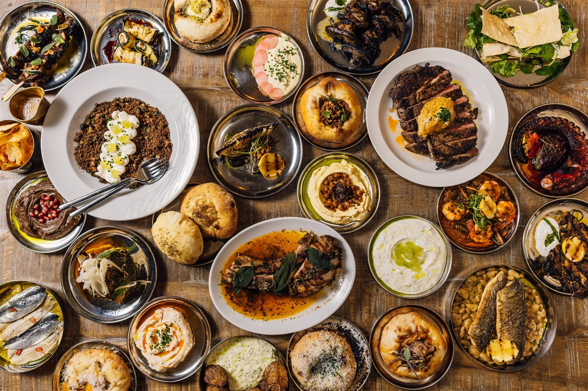 A variety of Middle Eastern dishes served on a wooden table, including grilled meats, hummus, salads, bread, and appetizers.