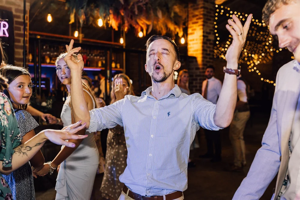 A wedding guest raising his hands and singing on the dance floor at White Syke Fields