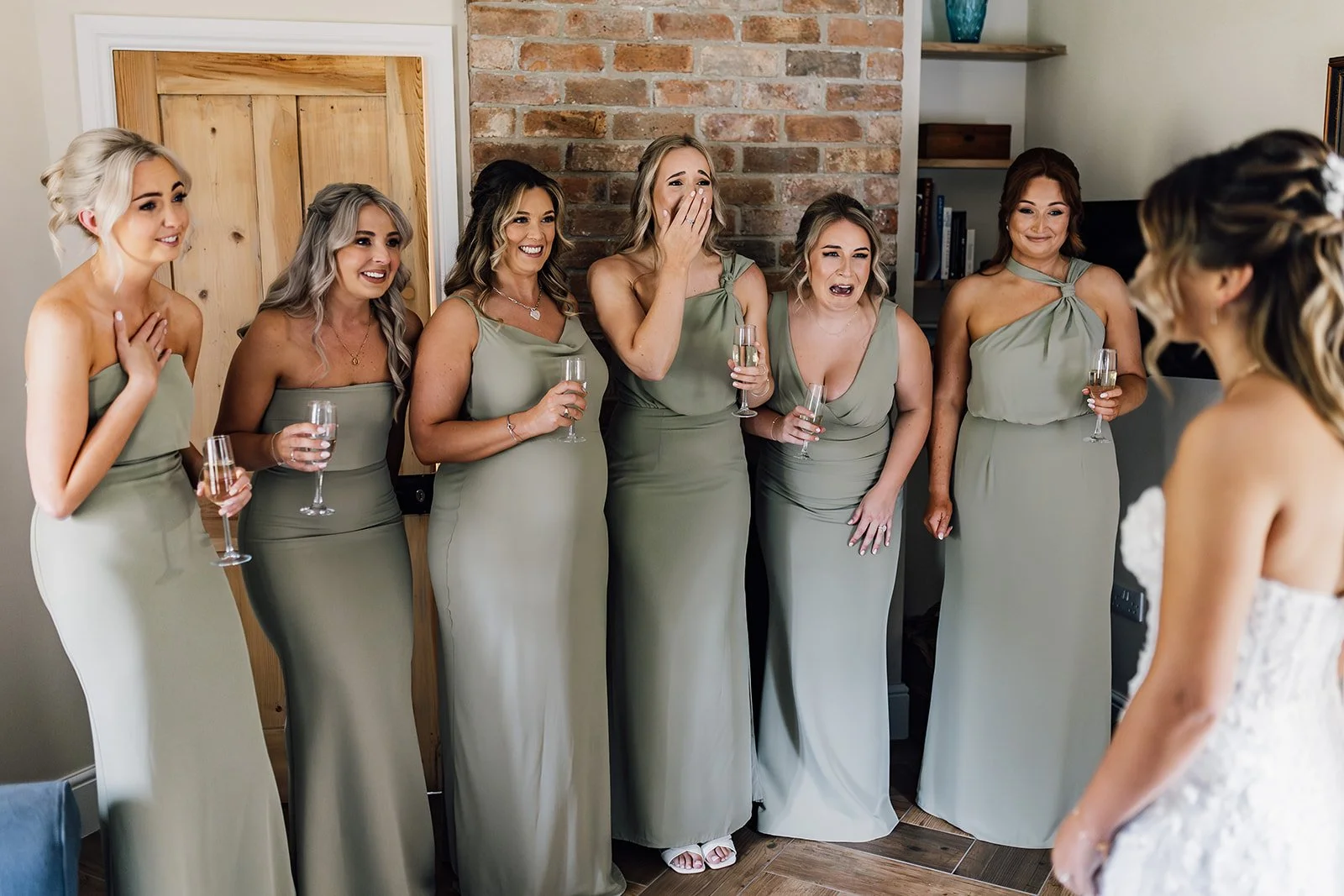 Bridesmaids in sage green dresses holding drinks before the ceremony