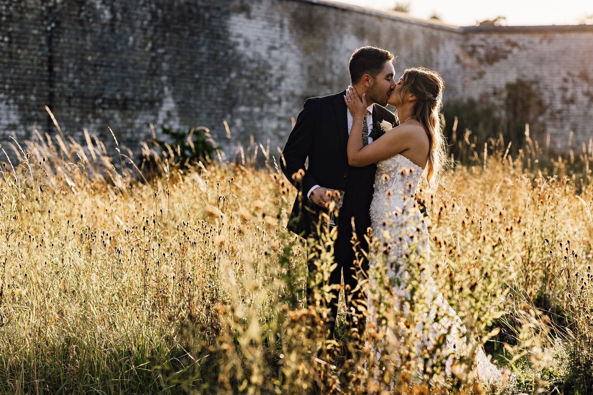 Charlotte and Rory kissing in golden evening light beside the walled garden at Scrivelsby