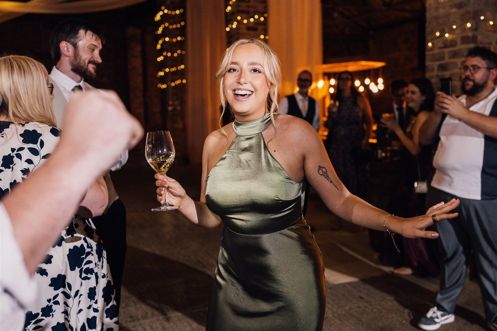 A bridesmaid laughing with a drink on the dance floor at White Syke Fields