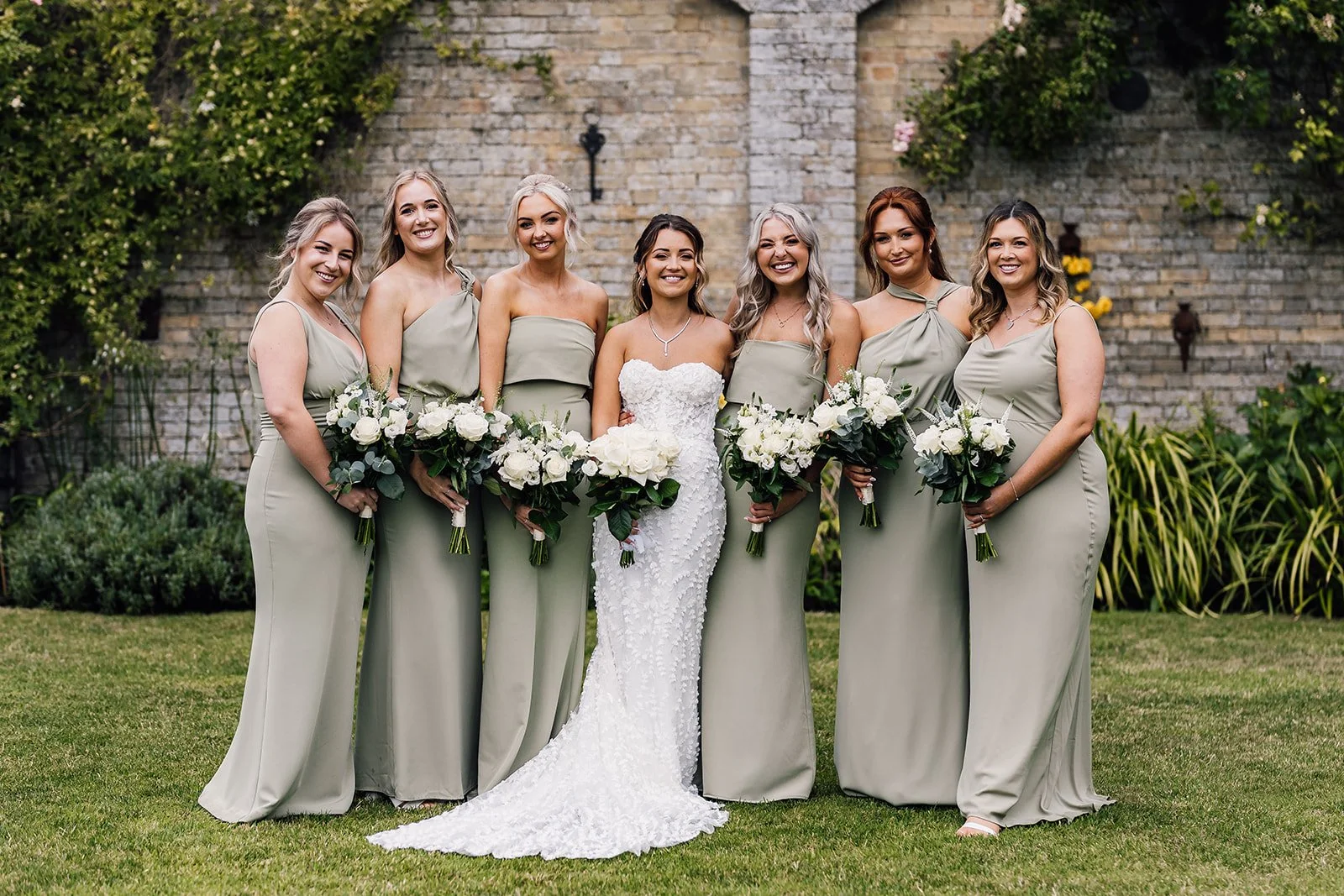Charlotte and her bridesmaids in sage green dresses beside the garden wall