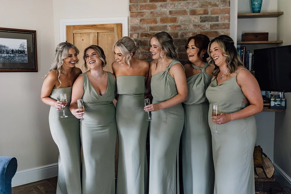 Charlotte laughing with her bridesmaids in sage green dresses before the wedding