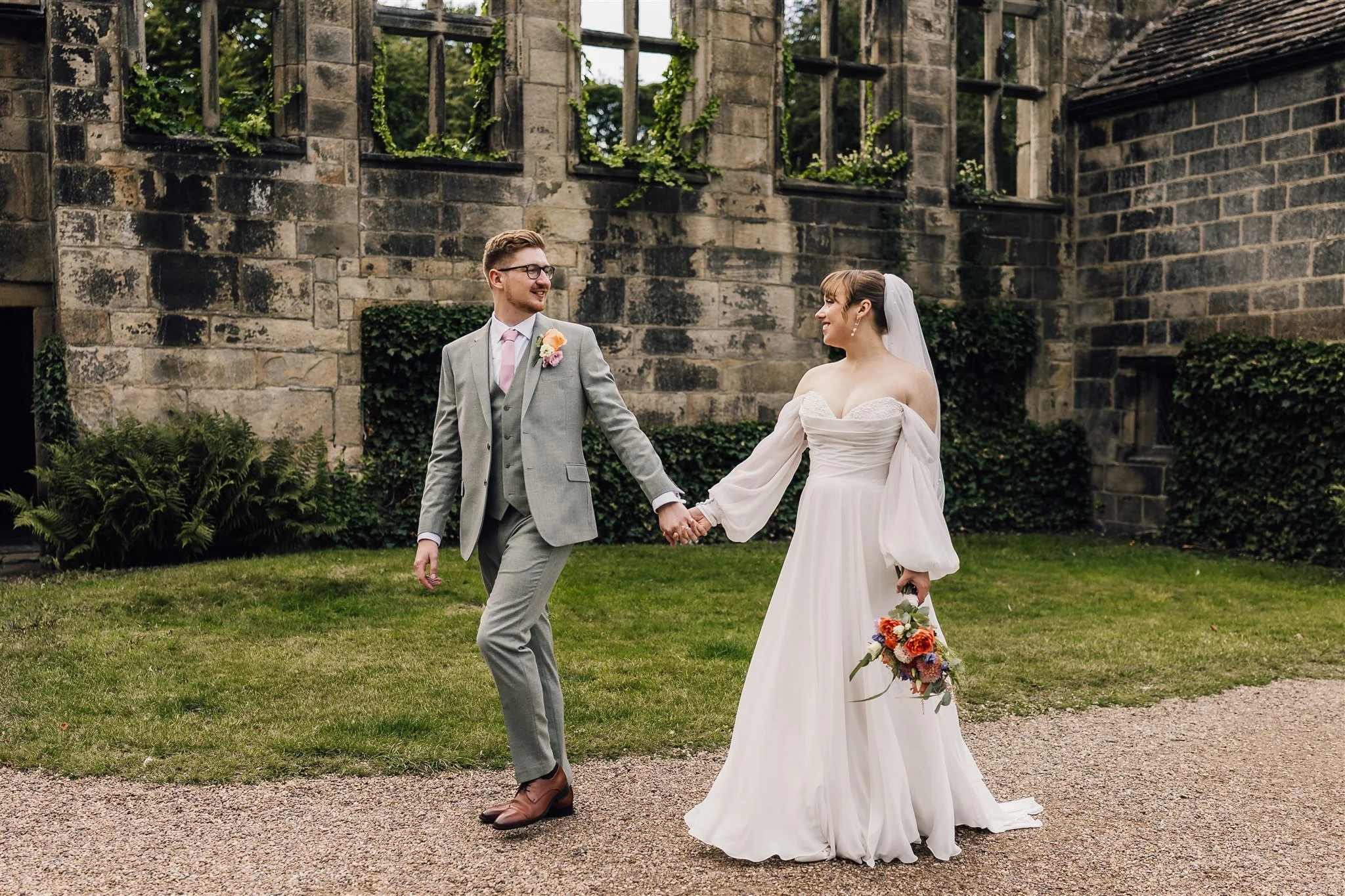 Bride and groom walking together at East Riddlesden Hall with historic stone building backdrop