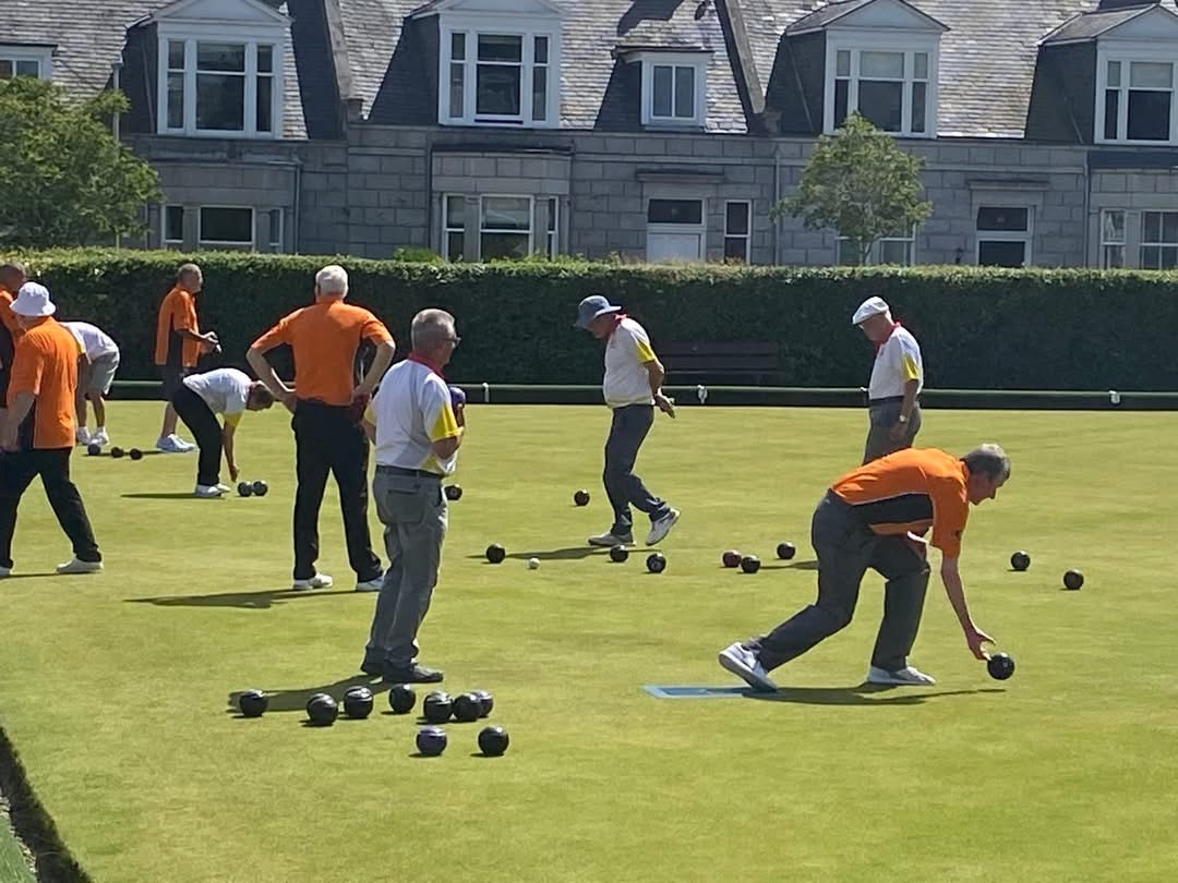 Lawn bowlers on a green playing a game in orange and white club shirts.