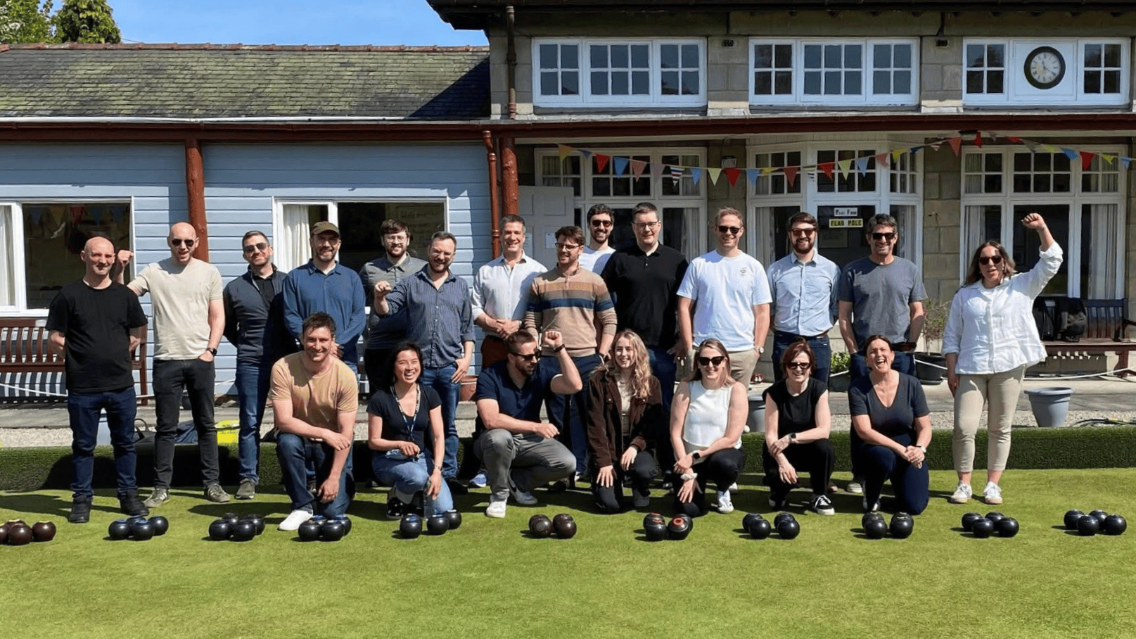 A group of people together outside a bowls club with bowls balls in front of them.