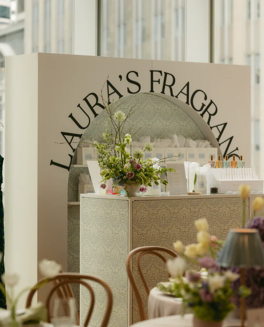 Display with a floral arrangement and skincare products in a bright, elegant setting, with the words "Laura's Fragran" visible on a sign in the background.