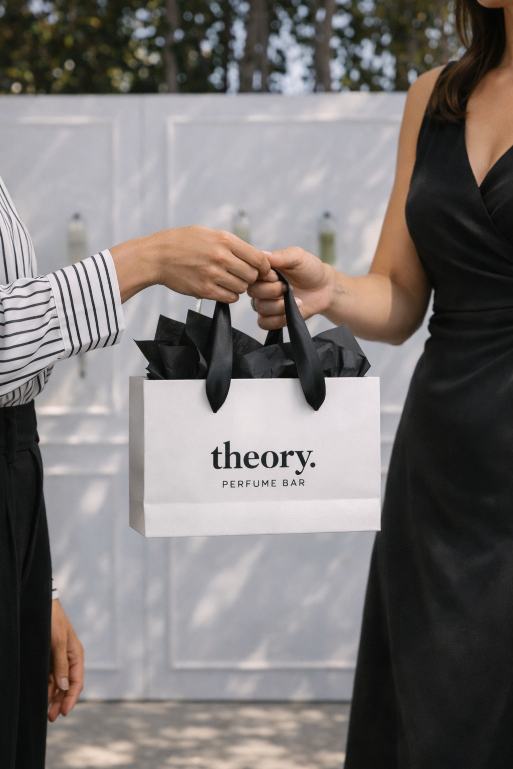 Two women exchanging a shopping bag from theory. perfume bar at an outdoor event.