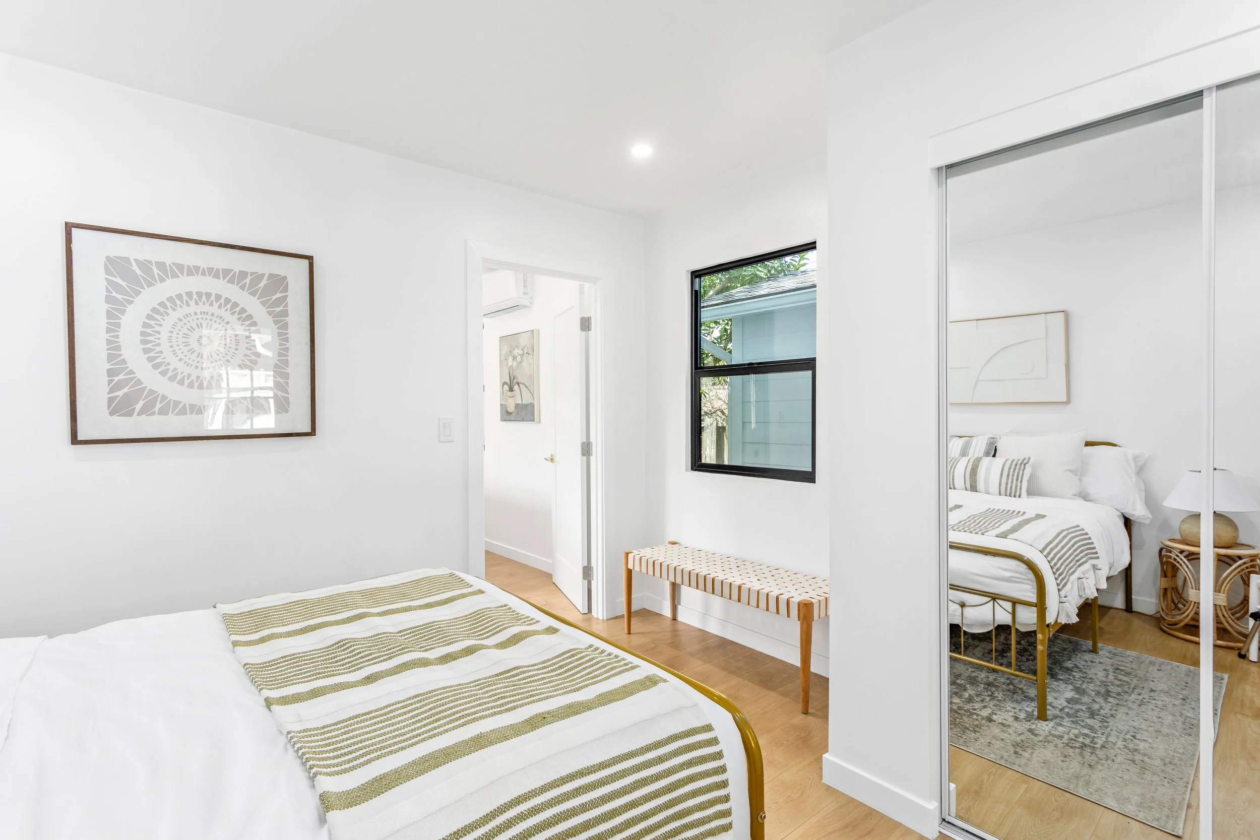 A bedroom with a bed, a mirrored closet door, a window, and minimalistic decor.