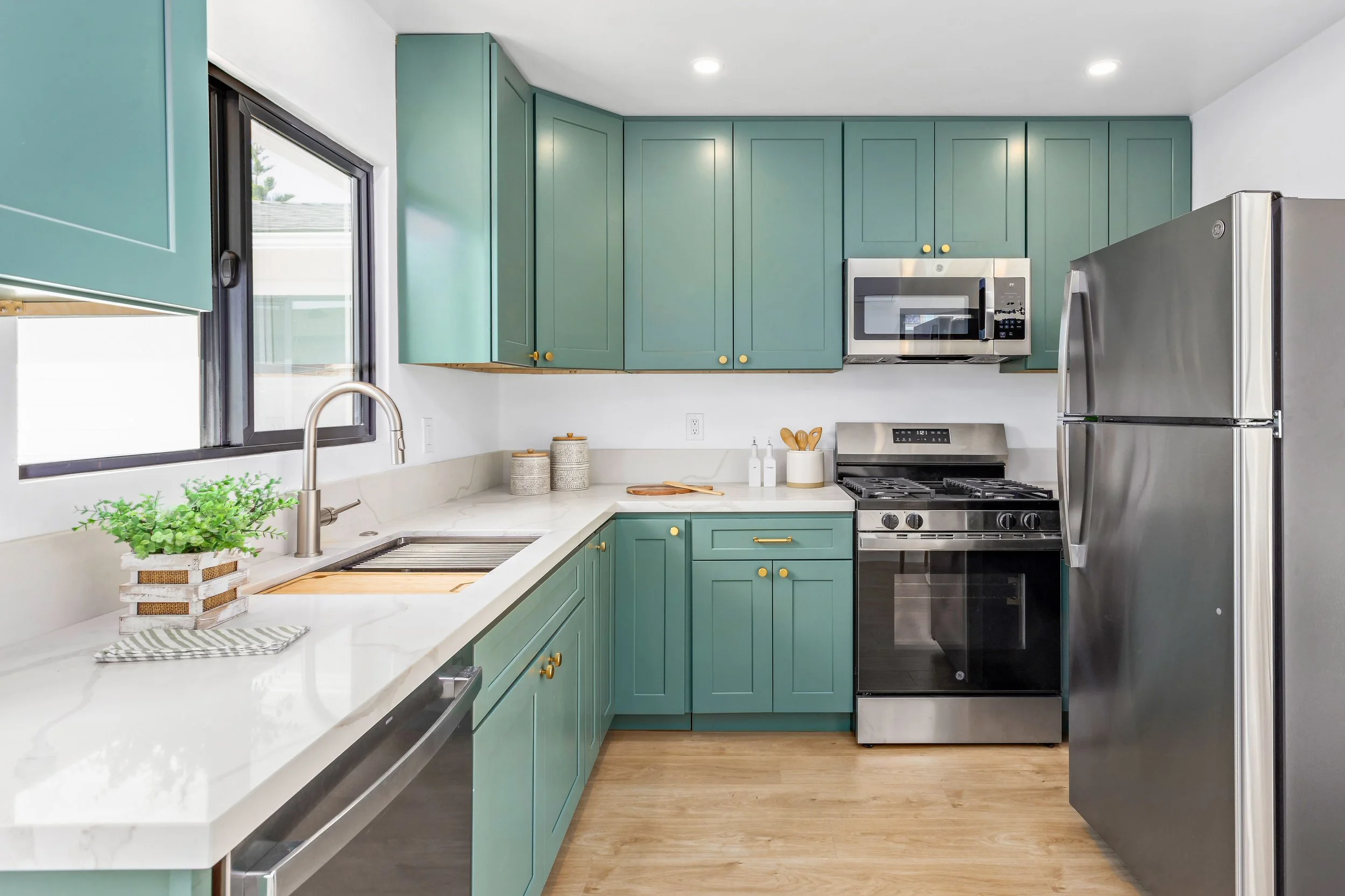 Modern kitchen with green cabinets, stainless steel appliances, a white marble countertop, and hardwood flooring.