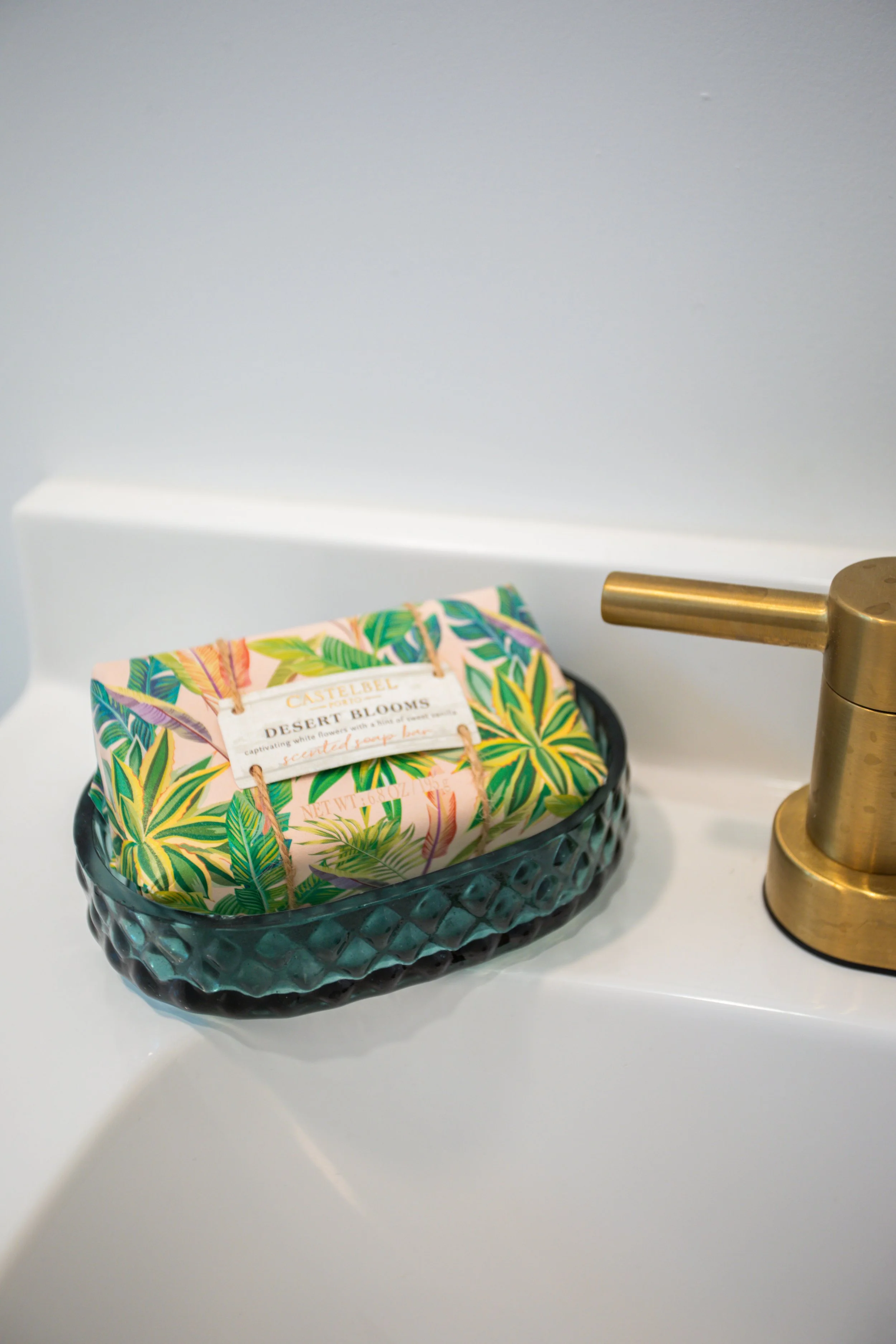 A bar of soap with a colorful desert blooms floral design in a black glass dish next to a gold-colored faucet on a white bathroom sink.