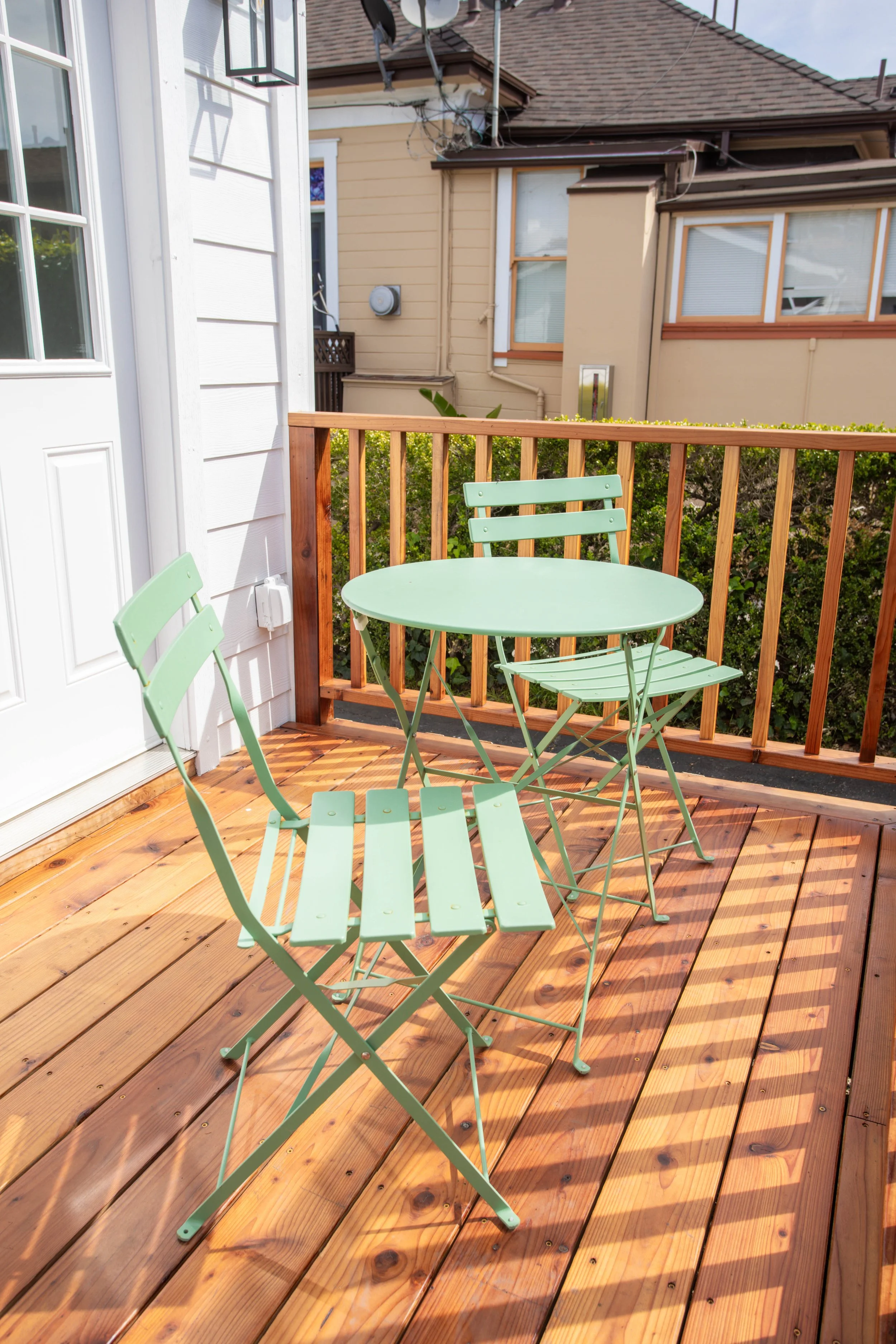 A wooden deck with a mint green metal patio table and two matching chairs.