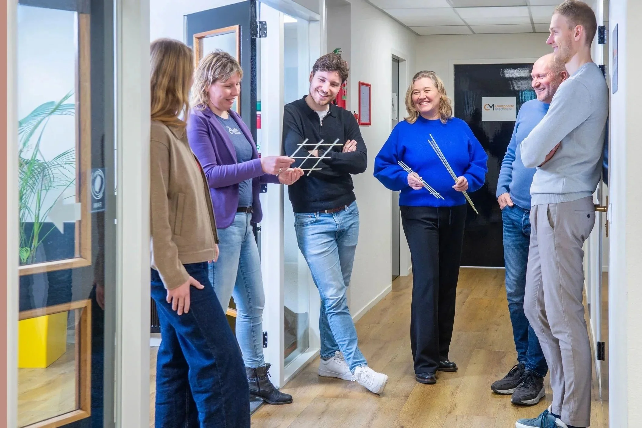 Group of six people standing in hallway, smiling and talking, some holding composite rebars
