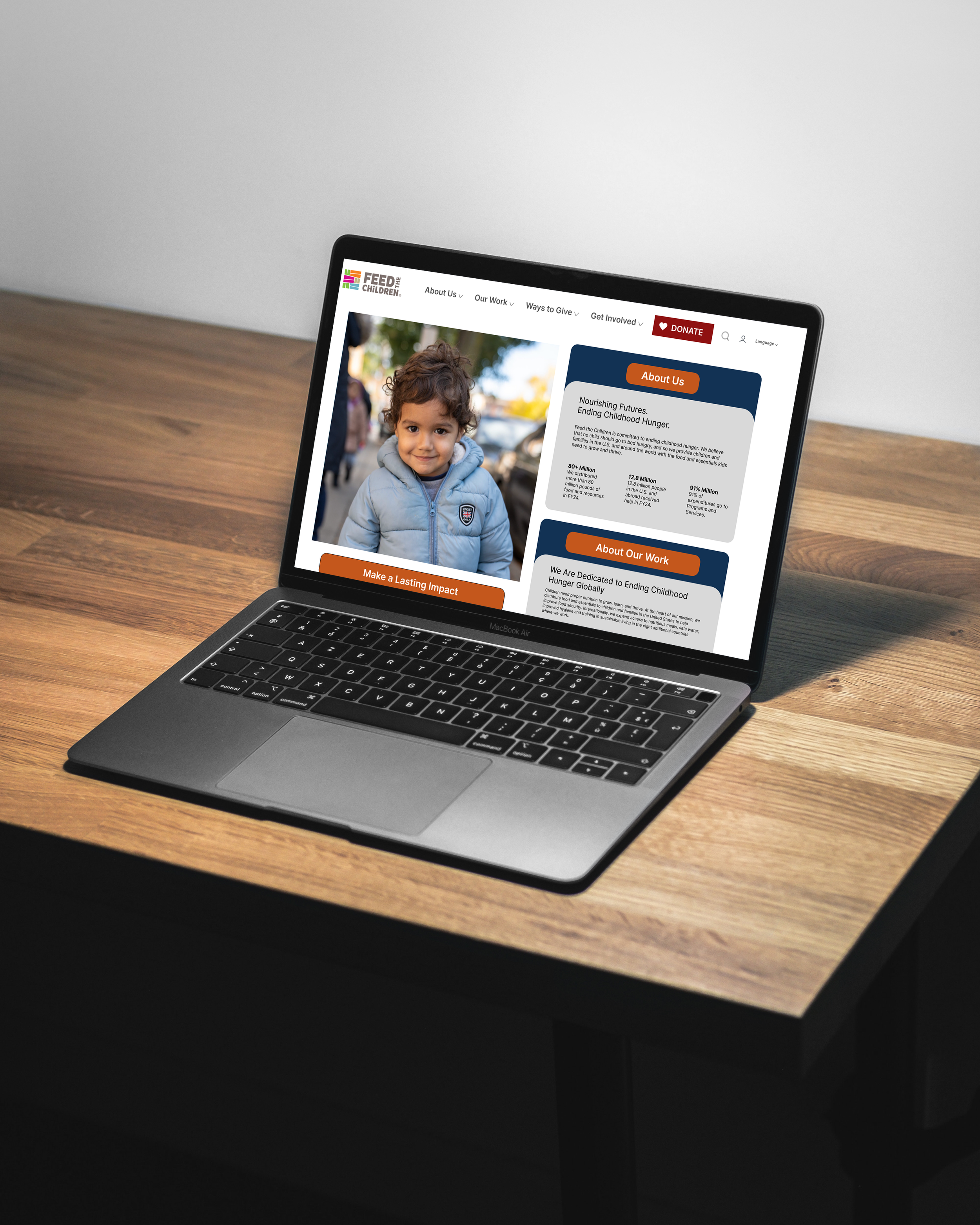 Laptop on a wooden desk displaying a website for Feed The Children, featuring a young boy in a gray jacket, with sections about their mission and work to end childhood hunger.
