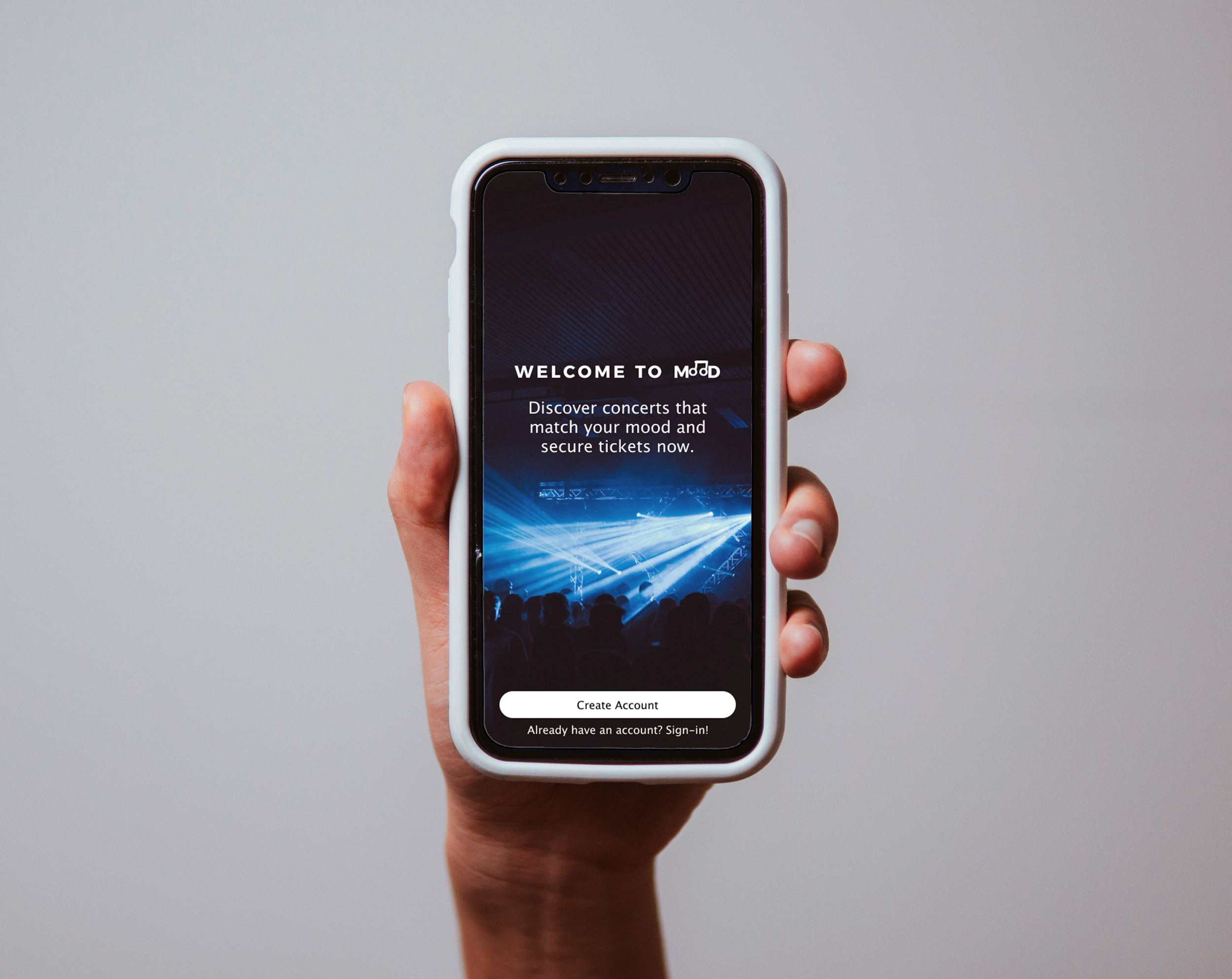 Hand holding a smartphone displaying a concert ticketing app with a blue concert scene and login options.