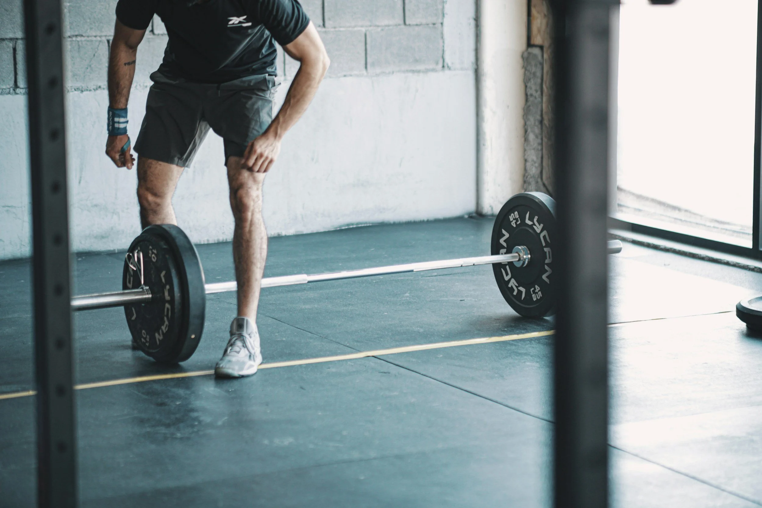 Homme en short et t-shirt, en train de faire de l'haltérophilie avec une barre chargée de poids dans une salle de sport
