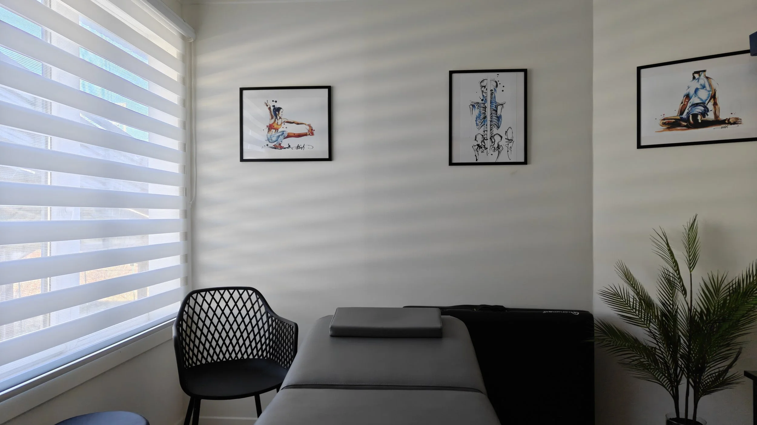 Une salle d'attente ou un bureau avec un fauteuil, un canapé, une plante, des tableaux d'art mural et des volets roulants laissant passer la lumière.