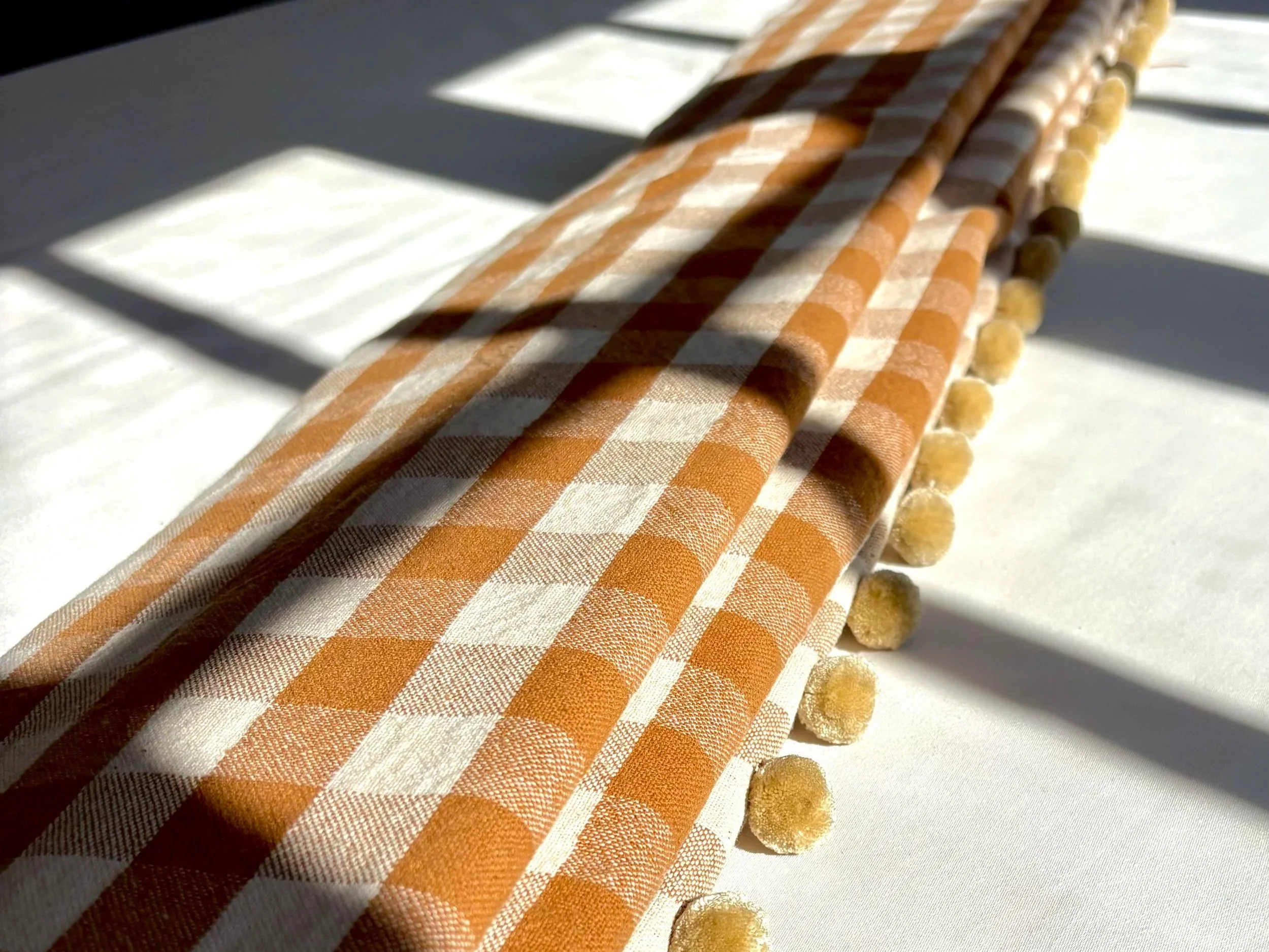 Close-up of orange and white checkered fabric straws with small cut pieces on a white surface, sunlight and shadows cast across the objects.