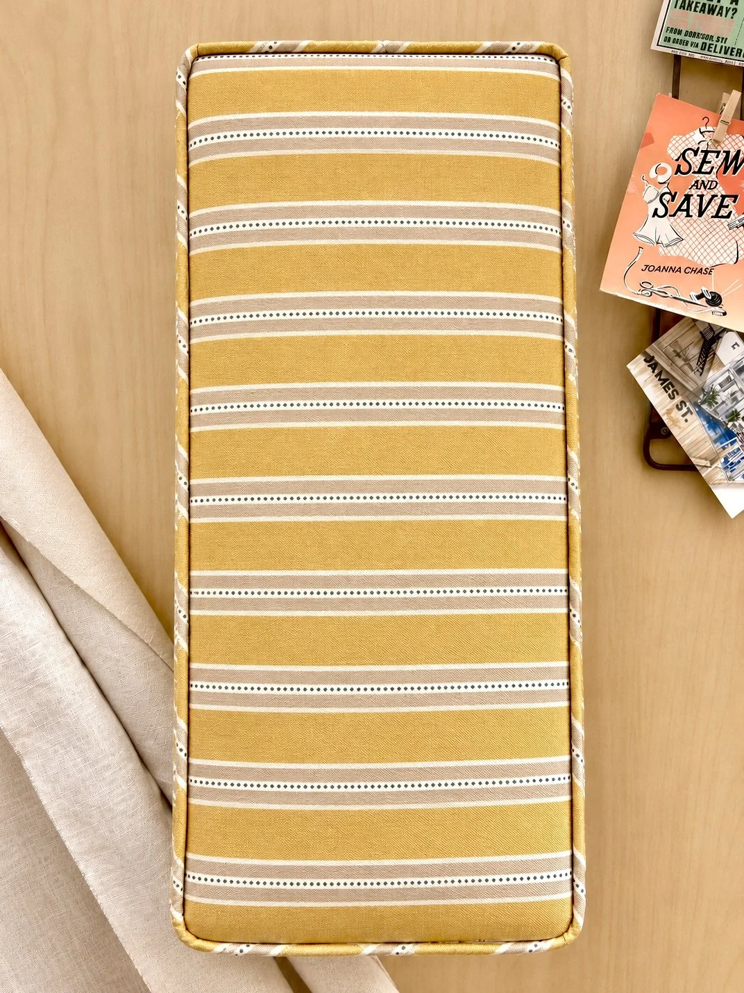A beige and yellow striped mattress or cushion with white and dark gray dotted lines, placed on a wooden surface.