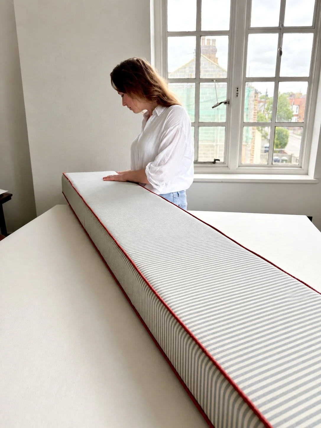 Woman inspecting a mattress in a bright room with large window