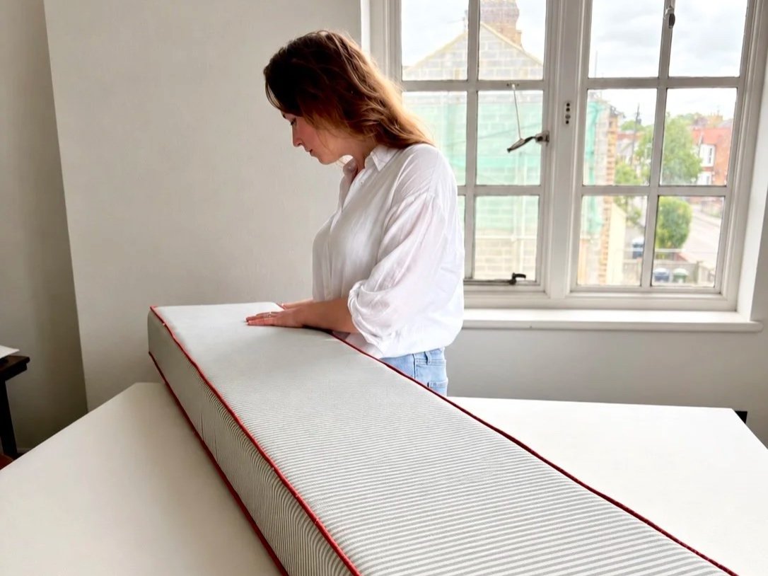 Woman in a white blouse examining a large air filter on a table in front of a window.