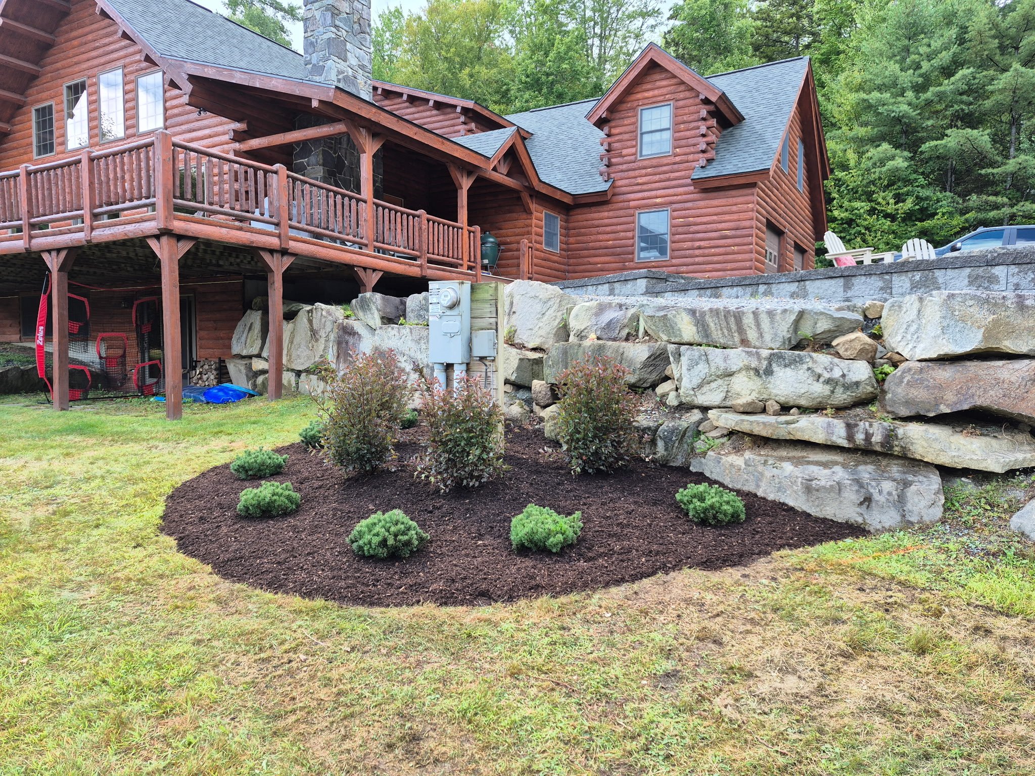 A wooden house with a deck and rock landscaping, with plants and mulch in the foreground.