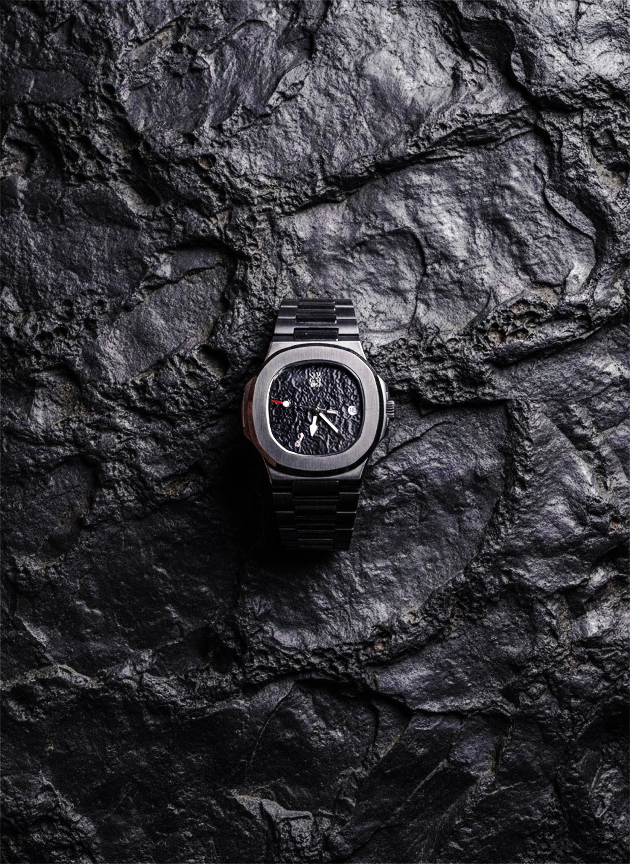A silver wristwatch with a black bracelet on a dark, textured stone surface.