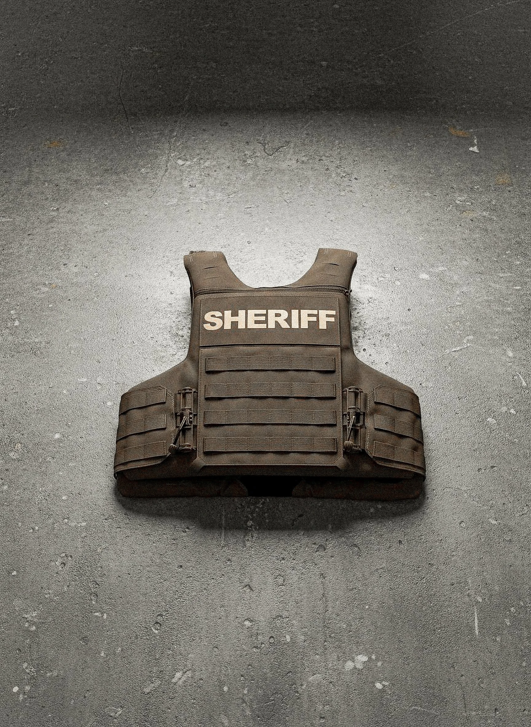 A brown sheriff's tactical vest with the word "SHERIFF" printed on it, laid flat on a concrete surface.