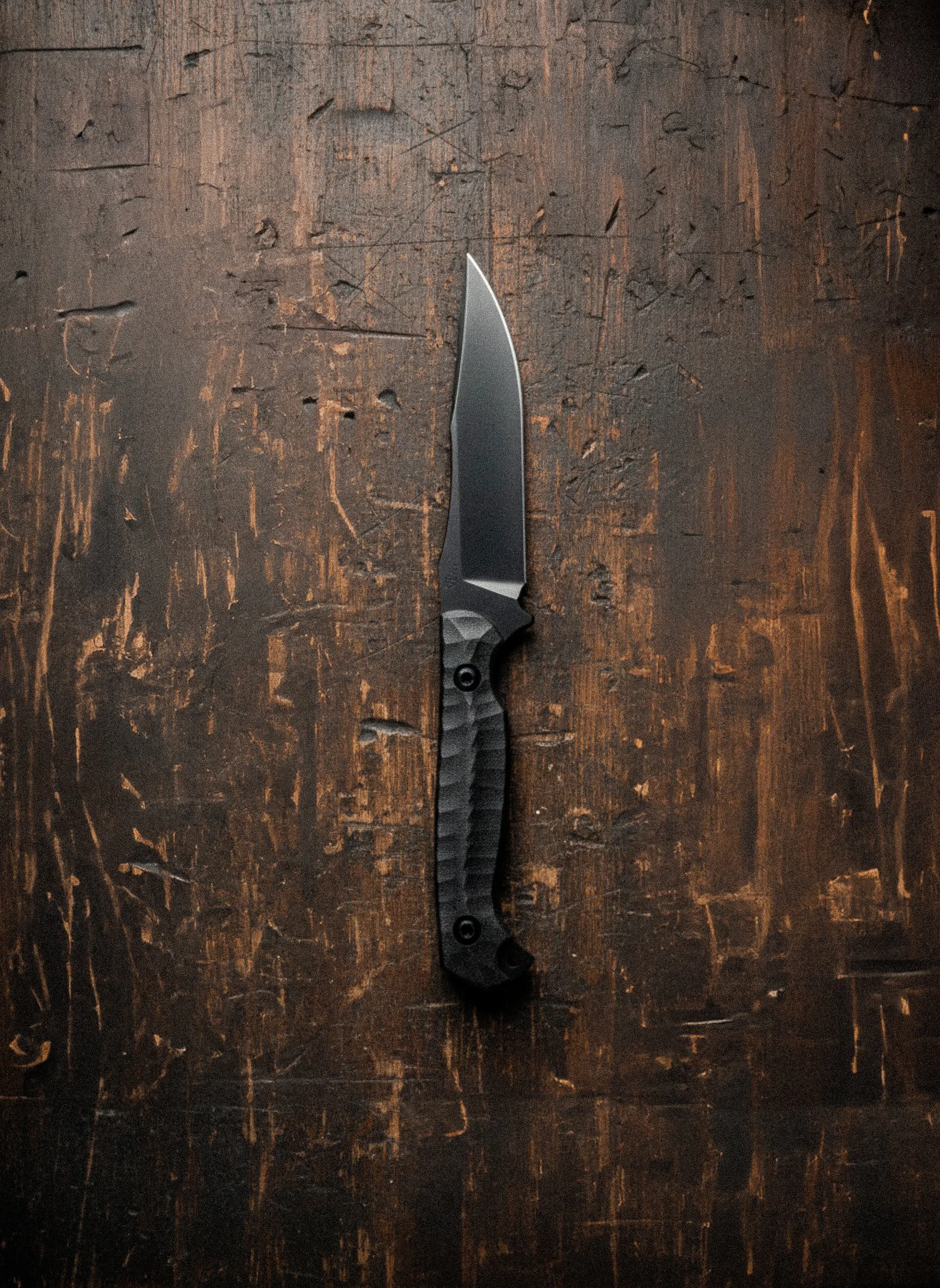 A black tactical folding knife placed on a dark, scratched wooden surface.