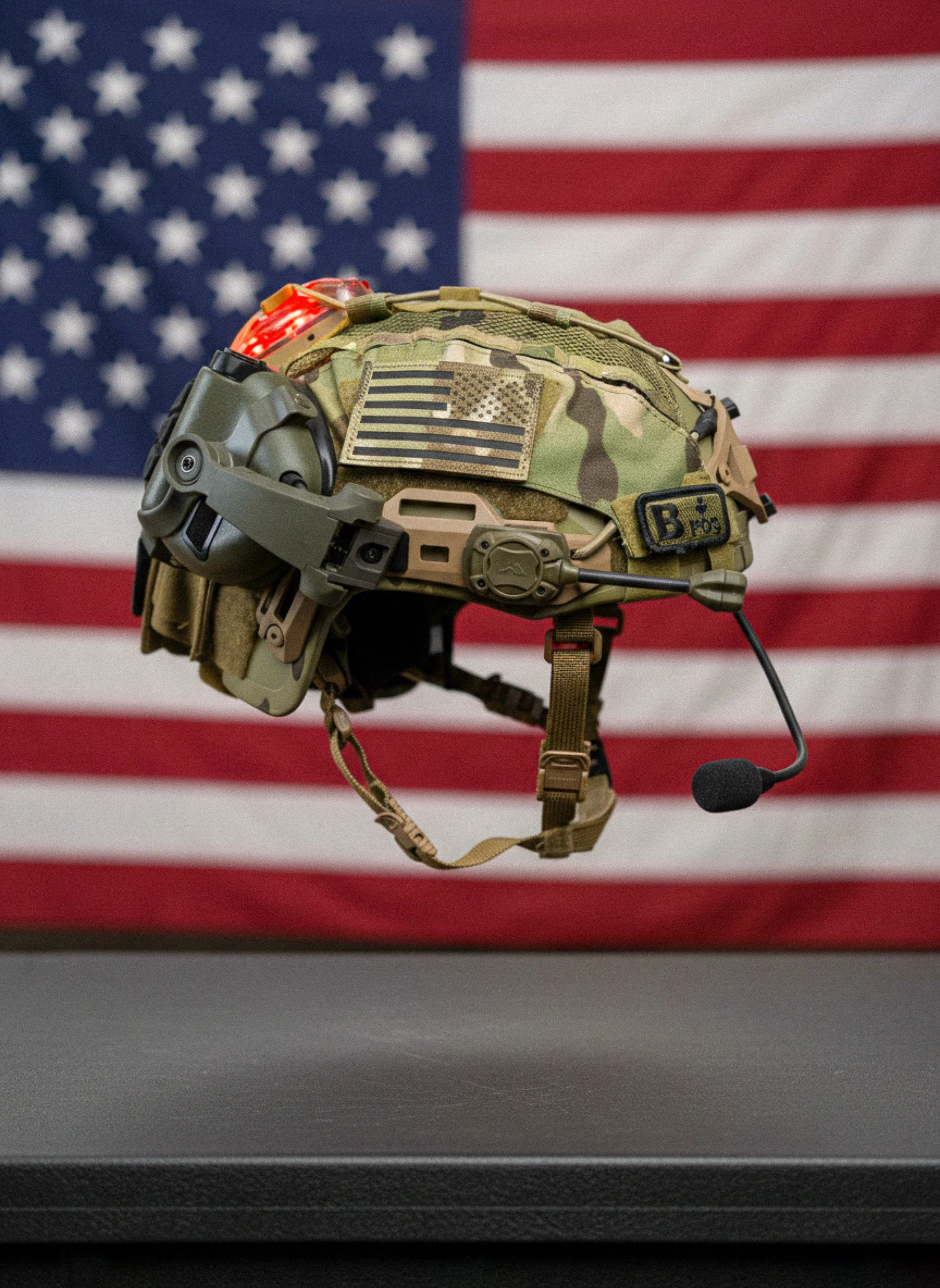Military helmet with a headset, microphone, and American flag patch, set against a background of the American flag.
