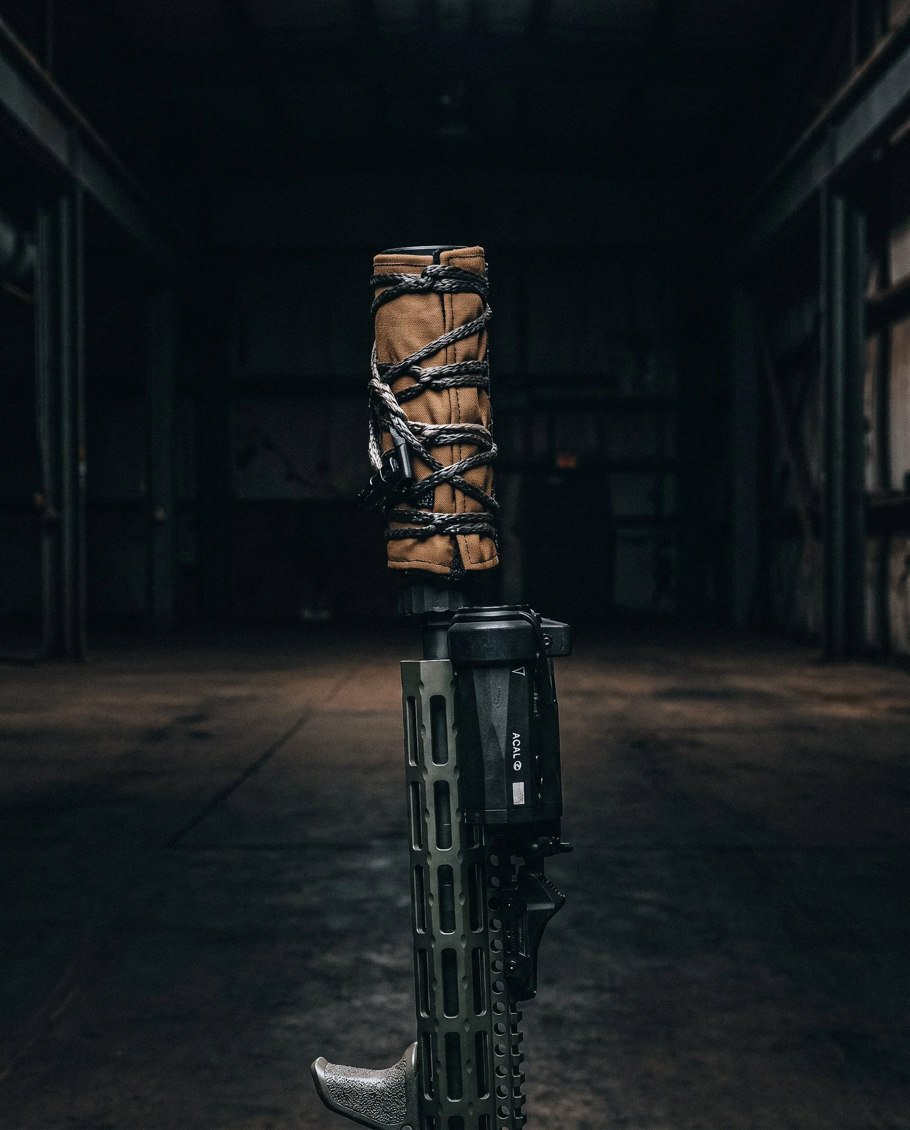 A tactical firearm with a brown grip and black accessories, mounted on a gun rest in a dark, empty room.