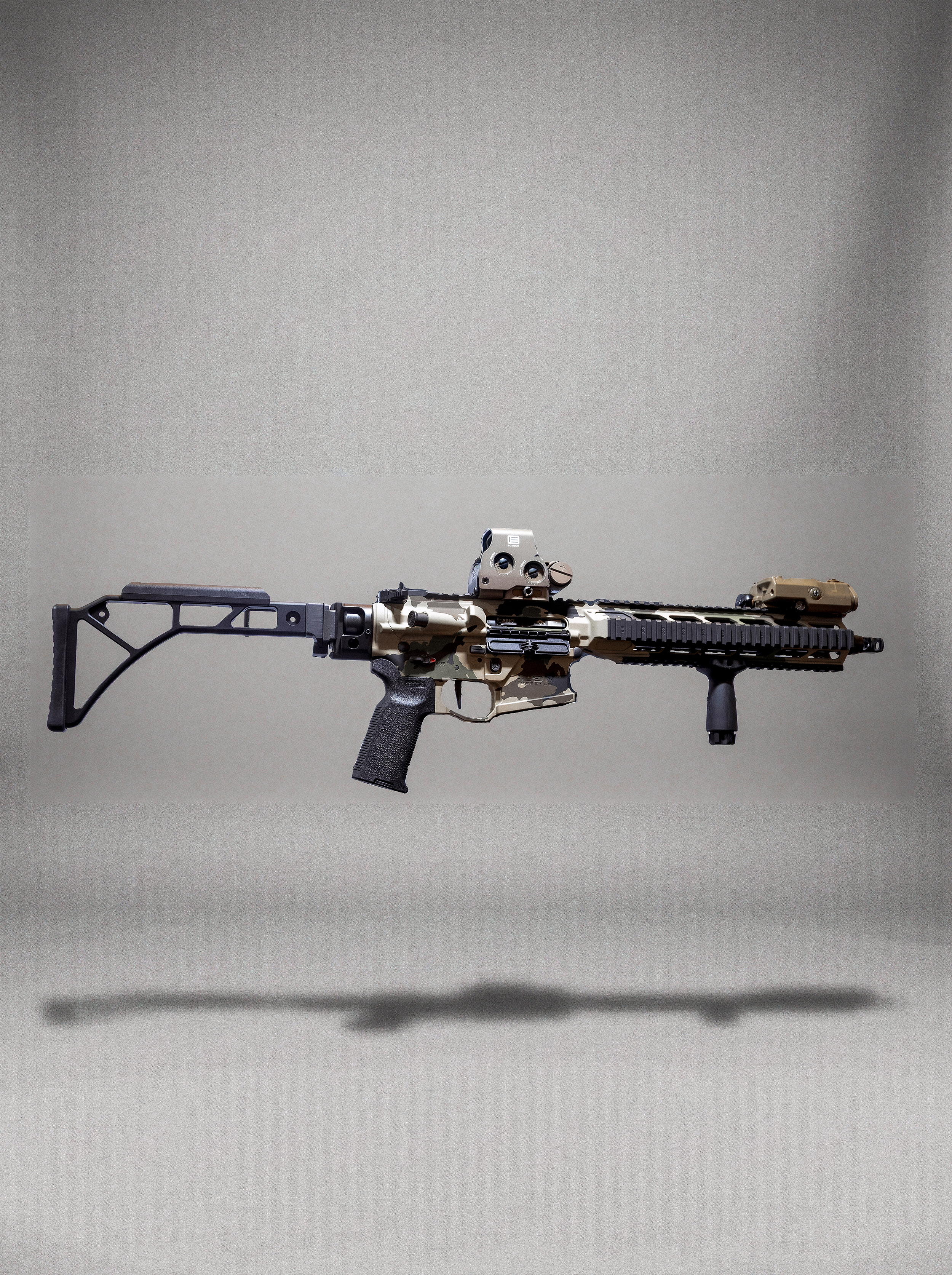A modern tactical rifle with camouflage pattern, mounted sights, and accessories, floating against a plain background.