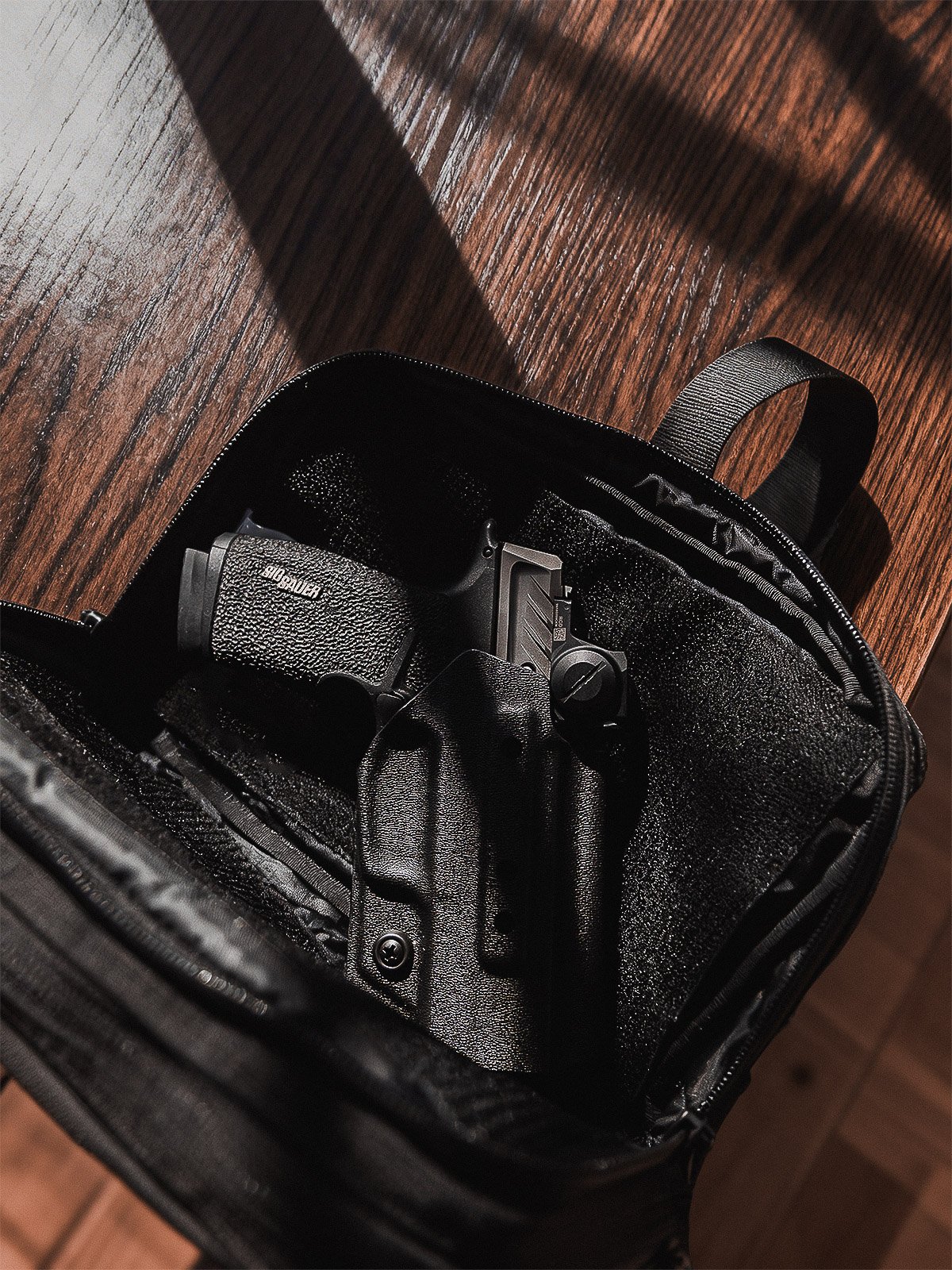 A firearm in a black case resting on a wooden surface, with a shadow cast over it.
