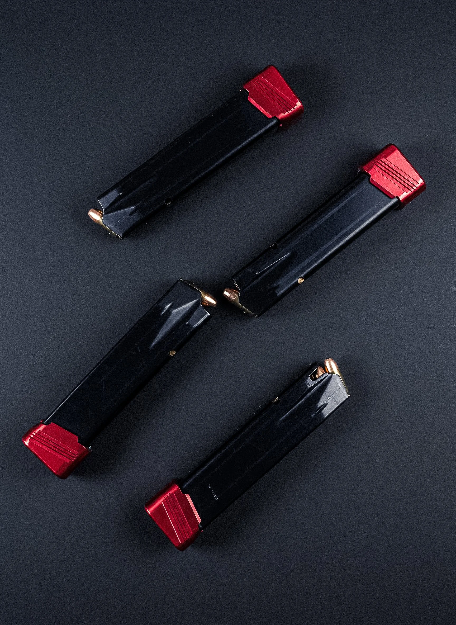 Four lipstick tubes with black bodies and red caps arranged in a diagonal pattern on a black surface.