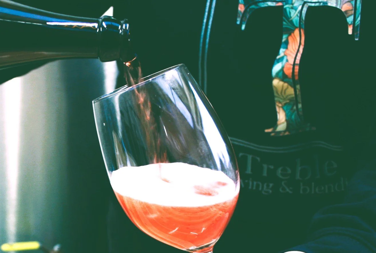 Pouring red wine into a glass with a floral patterned backpack in the background.