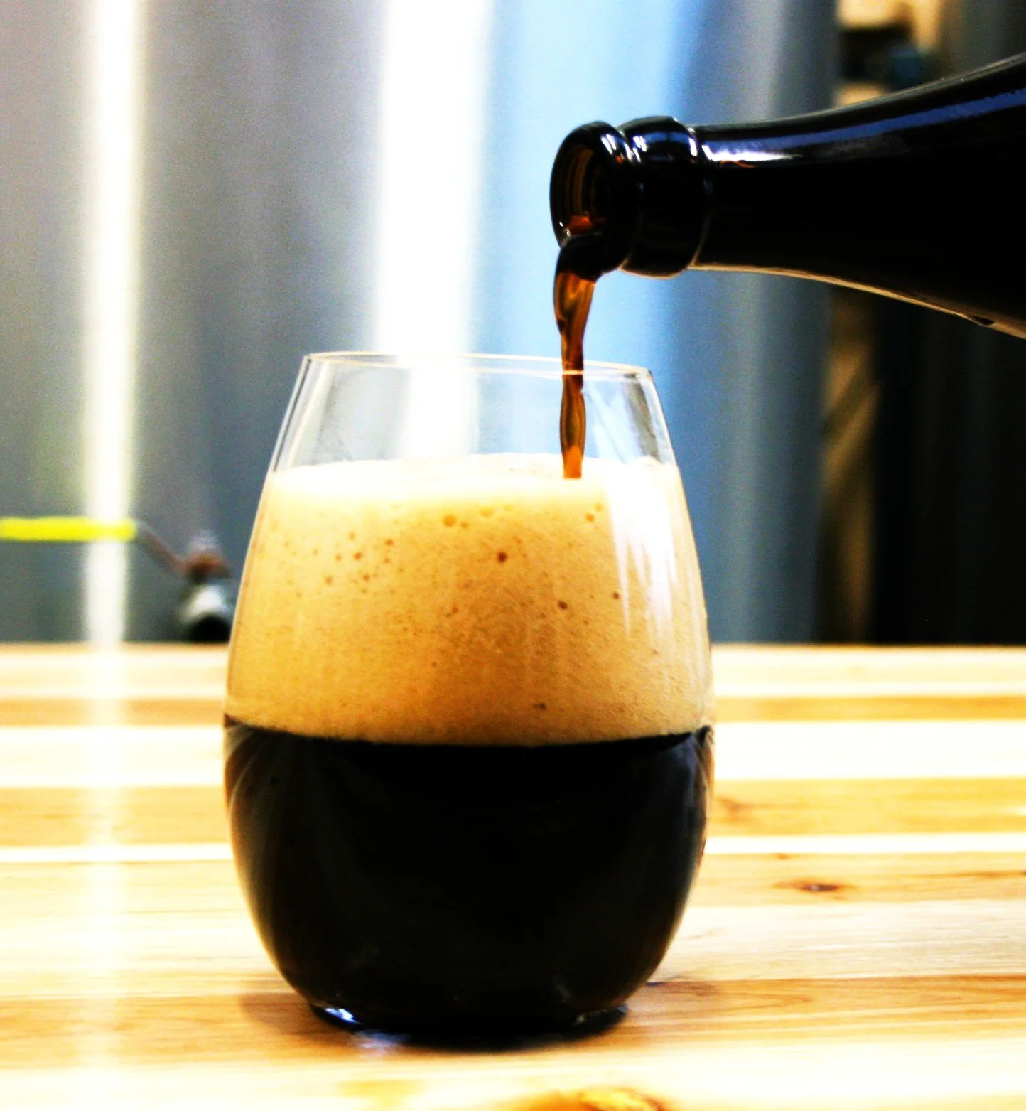A glass of dark beer with foam being poured from a bottle.