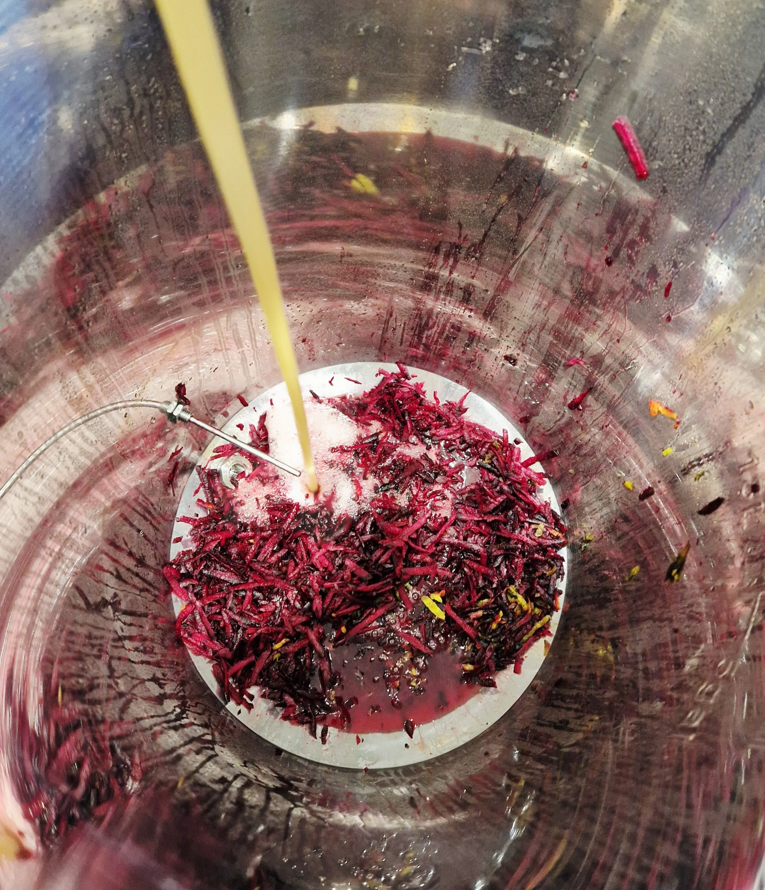 Inside a blender with purple and red shredded vegetables, some liquid, and a yellow straw.