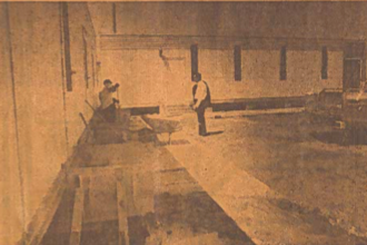 Two people sitting on a ledge and one person standing nearby in front of a building, in sepia tone.