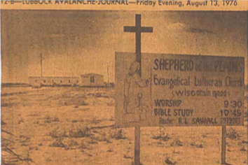 A church sign with a cross on top, advertising worship service times, and a nearby church building in the background.