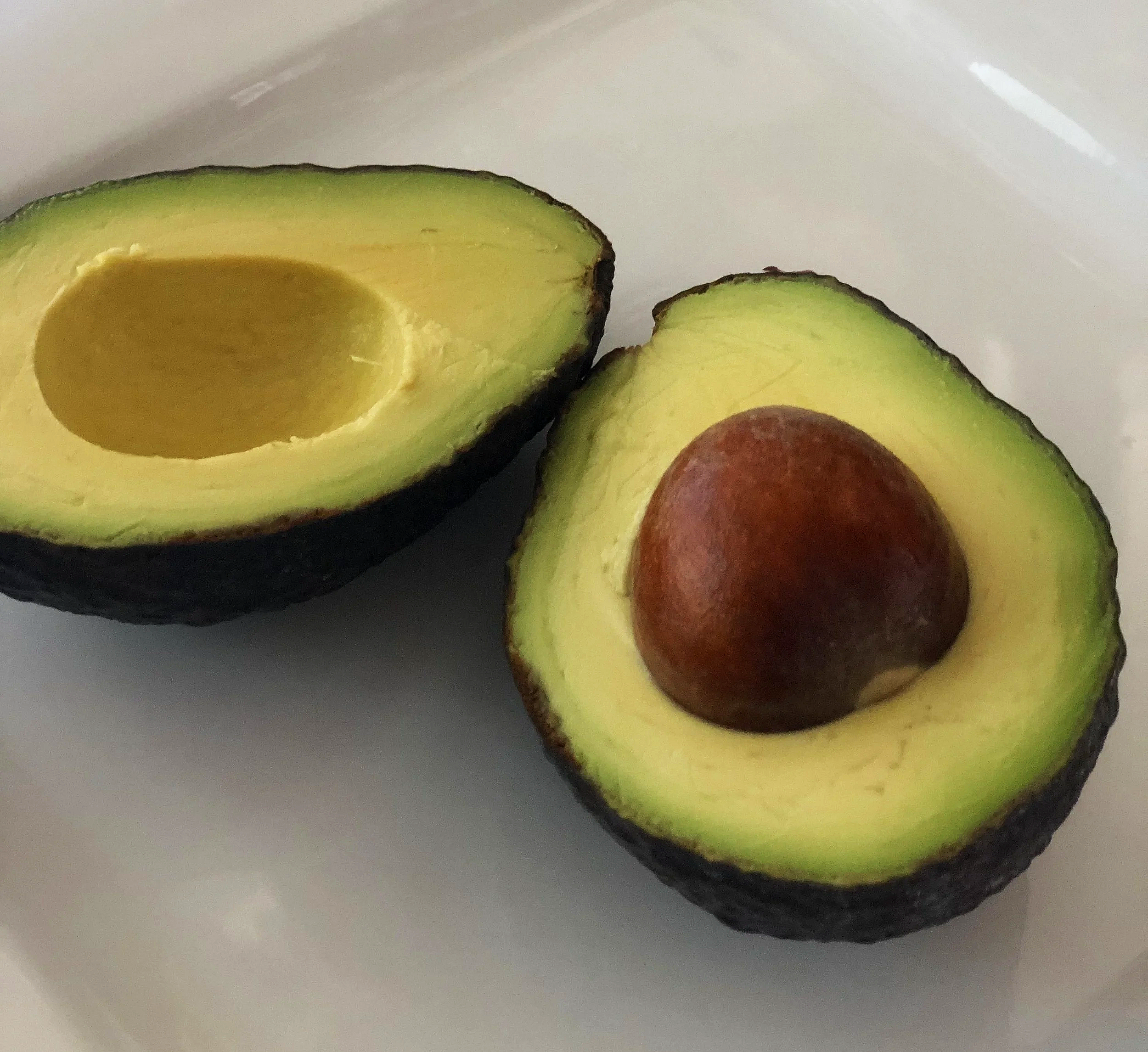 Close-up of halved avocado on a white surface, showing green flesh and brown seed.