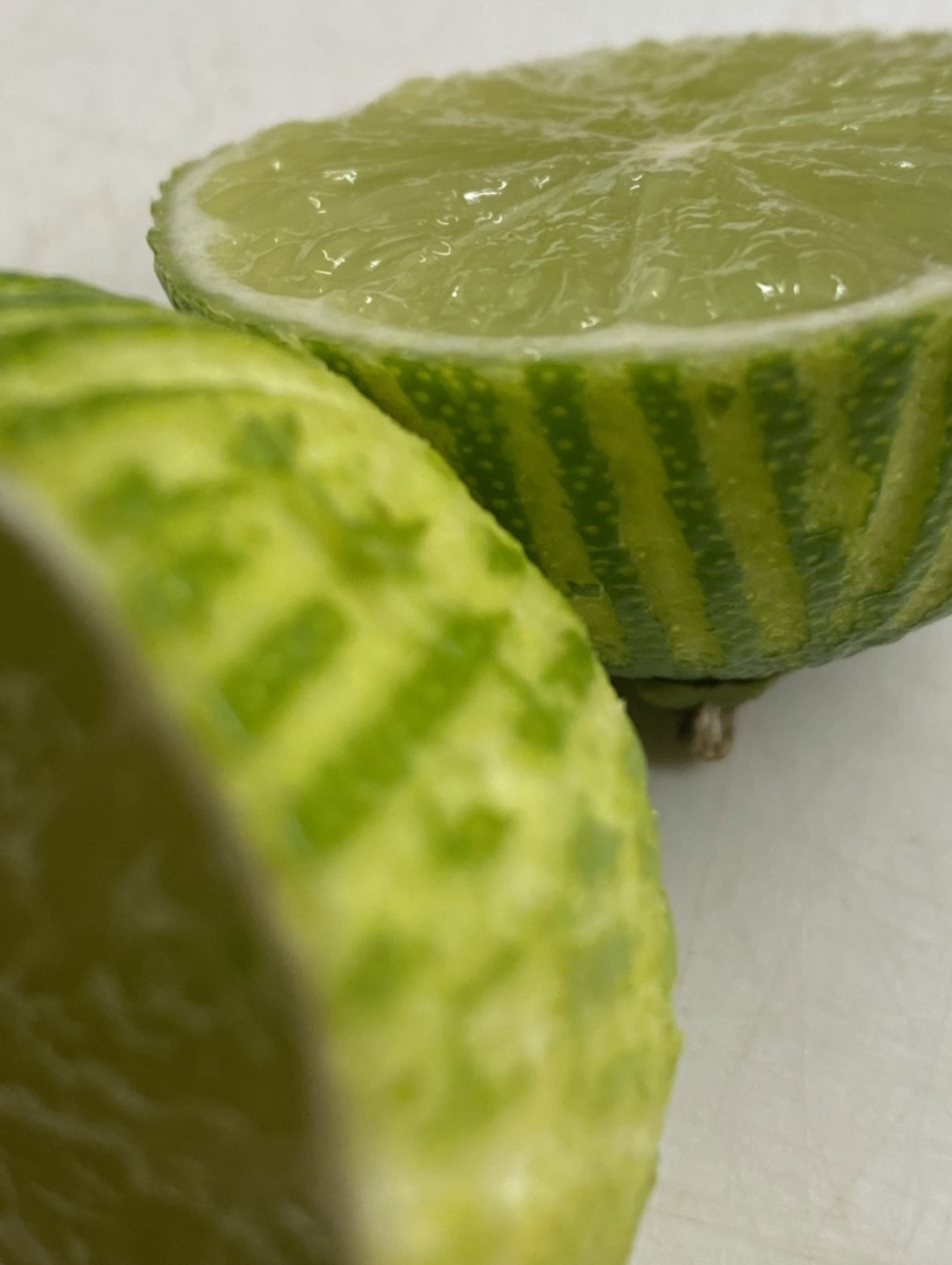 Close-up of a halved lime with green rind and juicy interior, and part of another lime in the foreground.