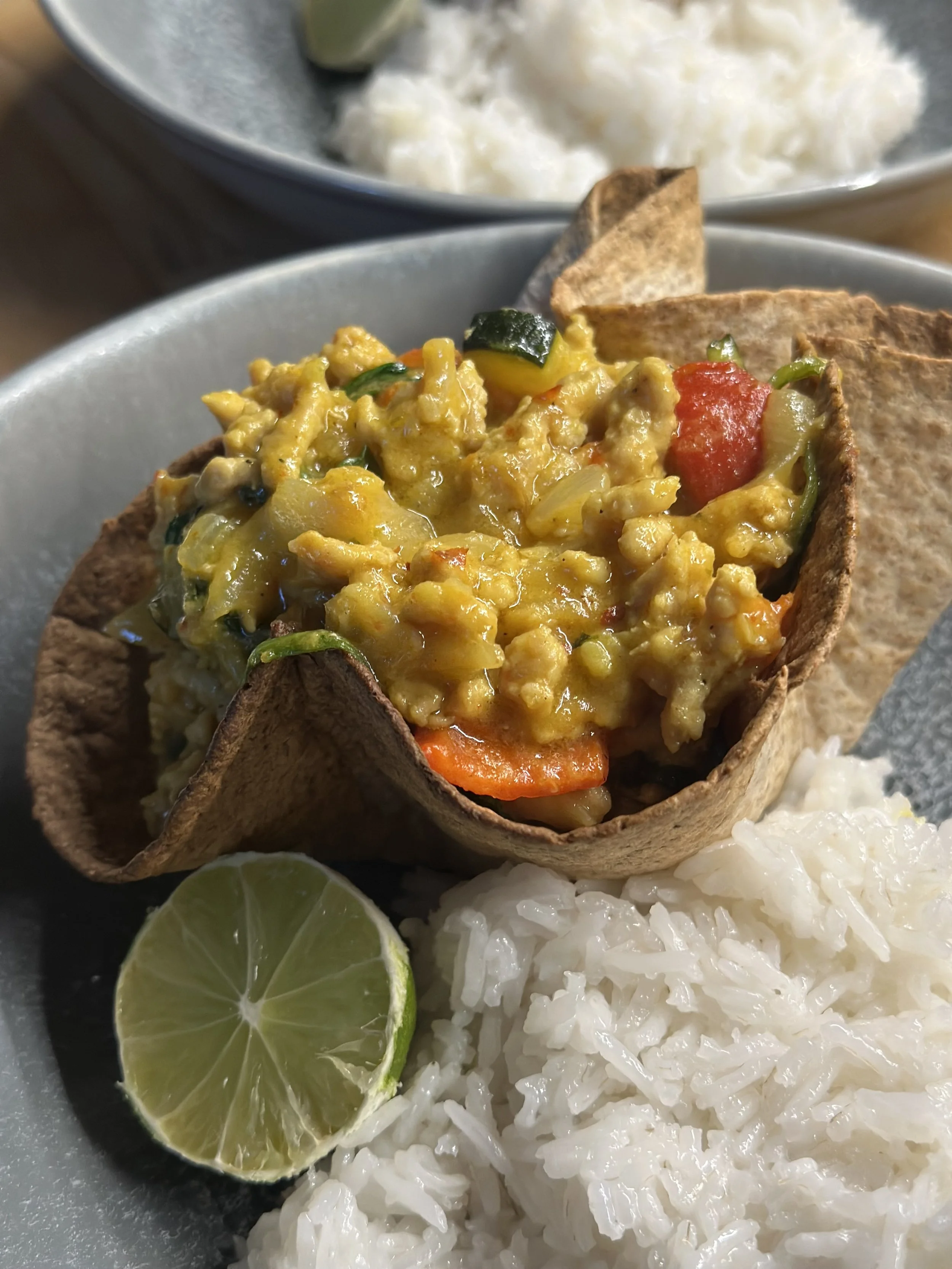 A skillet with rice, lime slices, and a taco filled with scrambled eggs, vegetables, and tortillas.