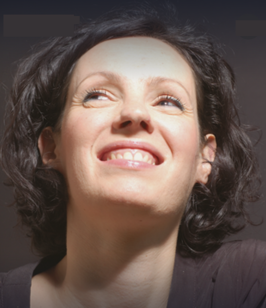 Close-up of a woman with short, curly dark hair smiling and looking slightly upward.