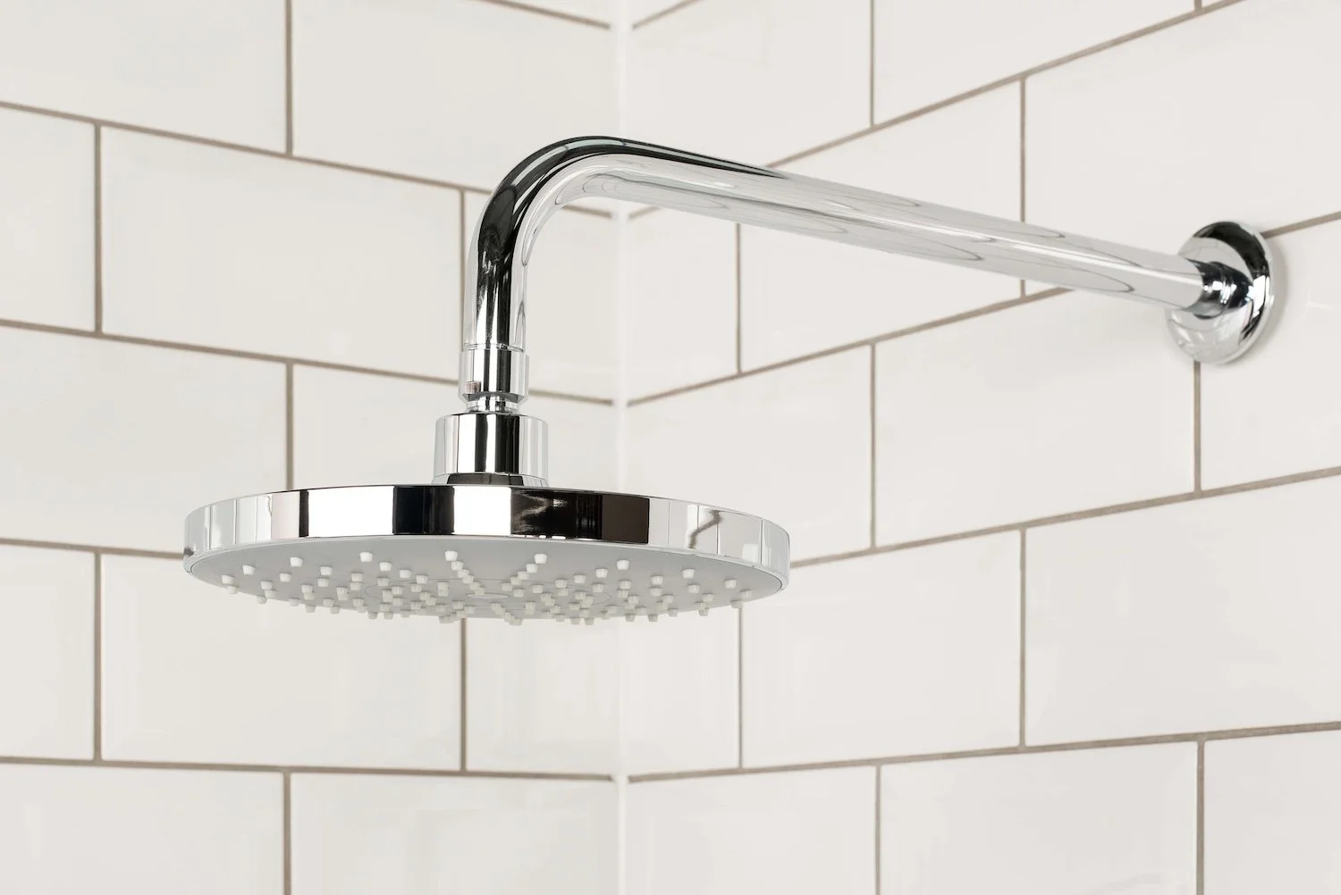 Chrome rainfall shower head on a wall arm against white metro tiles