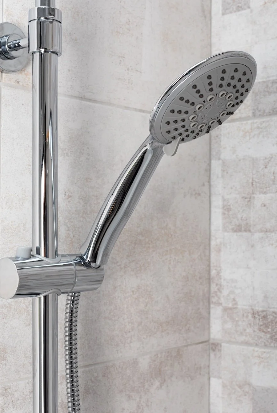 New chrome shower head and riser rail fitted against beige bathroom tiles