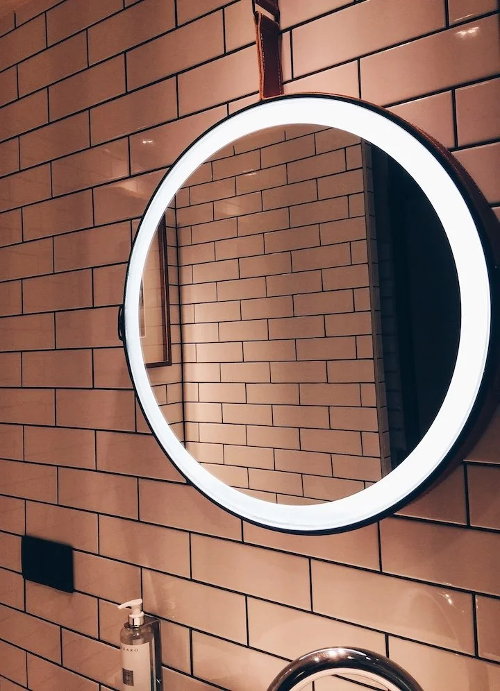 Round LED mirror hung on a leather strap against a metro-tiled wall