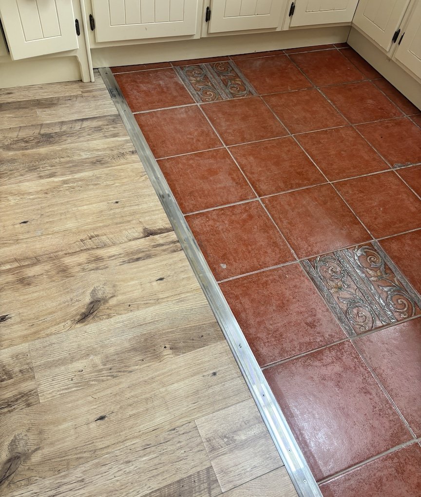 Metal transition strip joining wood-effect laminate to terracotta kitchen tiles